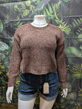 Mannequin wearing a brown knitted sweater and denim shorts against a leaf-patterned background