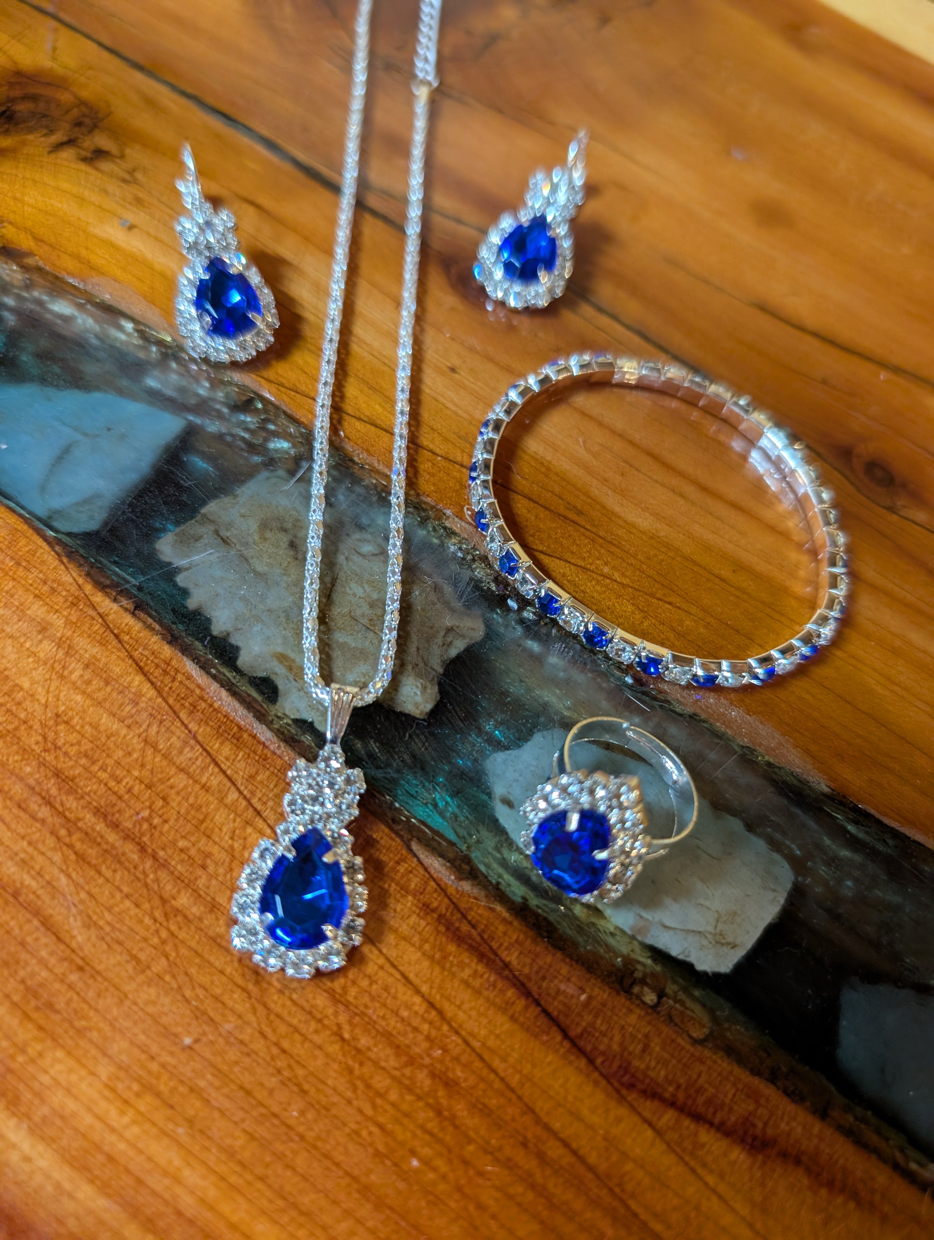 “Elegant 5-piece blue fashion jewelry set with necklace, earrings, bracelet, and ring on wood background.”