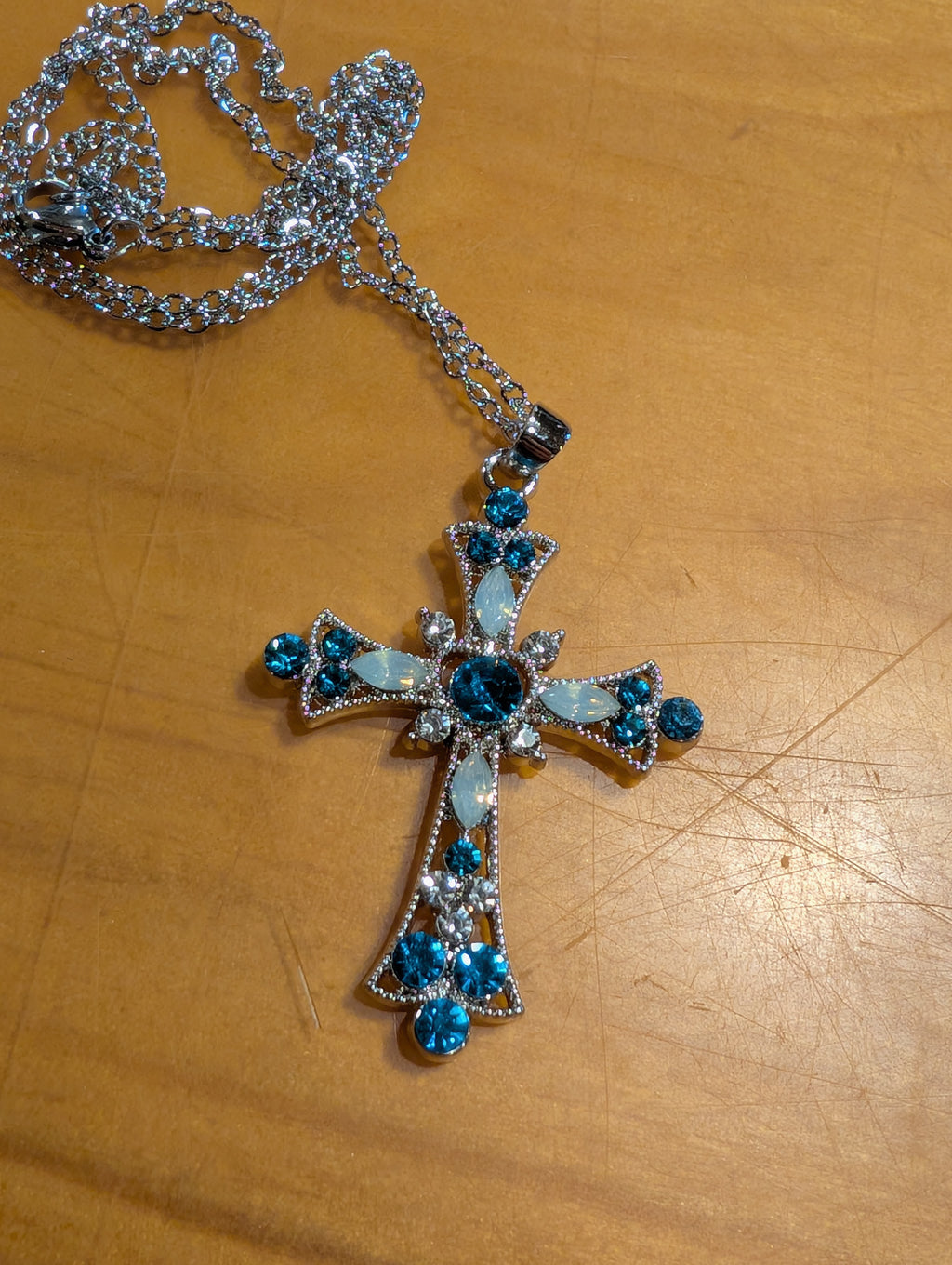 Silver cross pendant with blue stones on a wooden surface