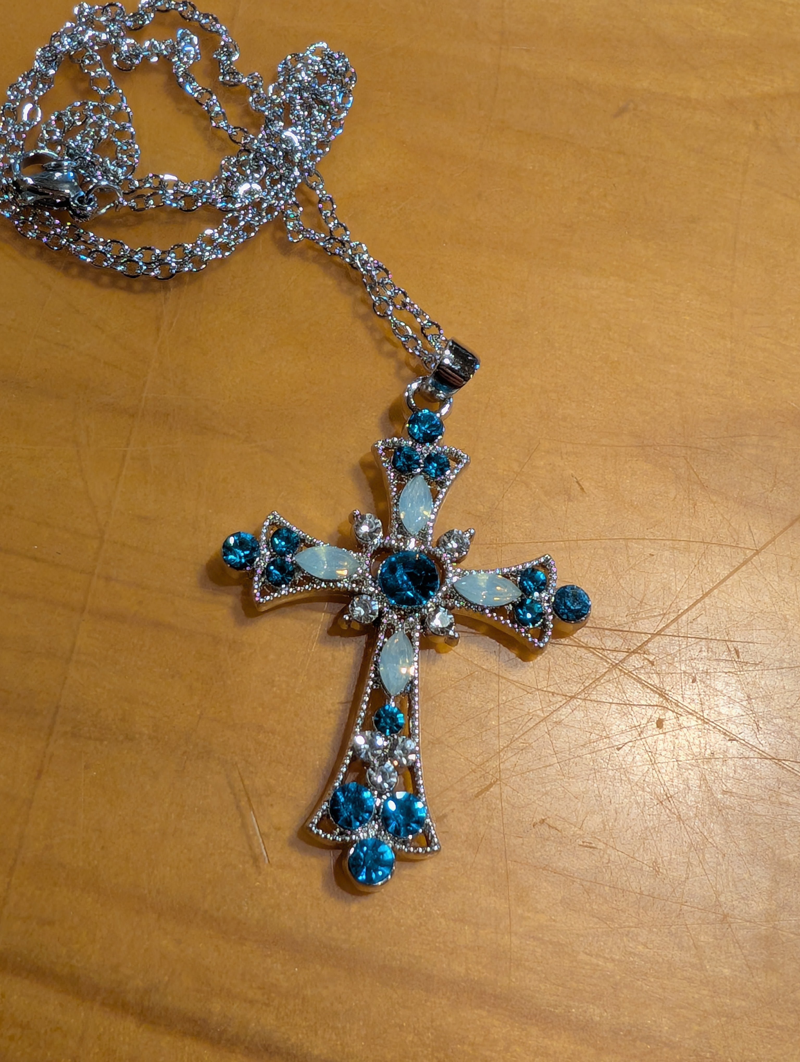 Silver cross pendant with blue stones on a wooden surface