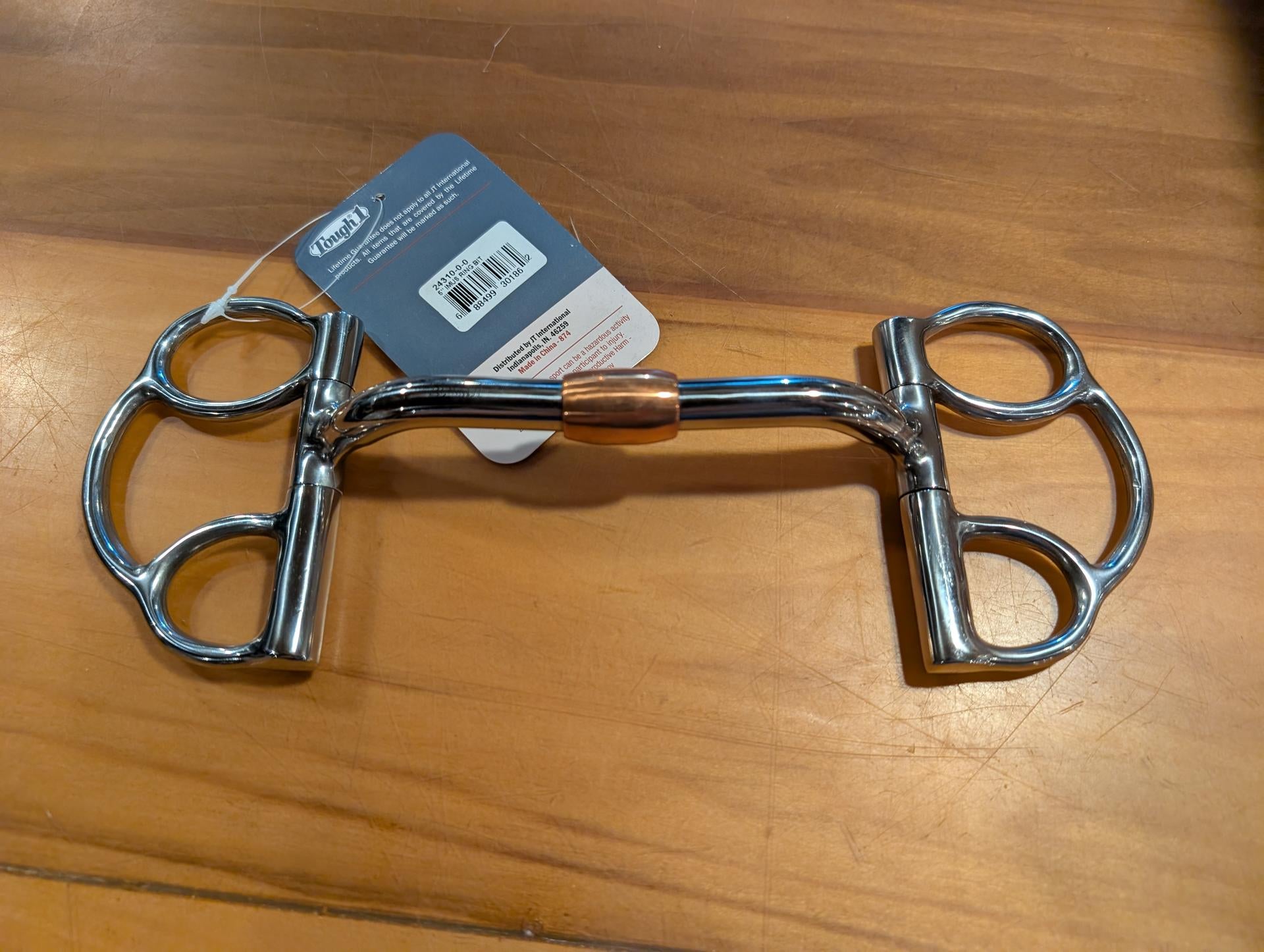 Metal horse bridle bit on a wooden surface with a brand label.
