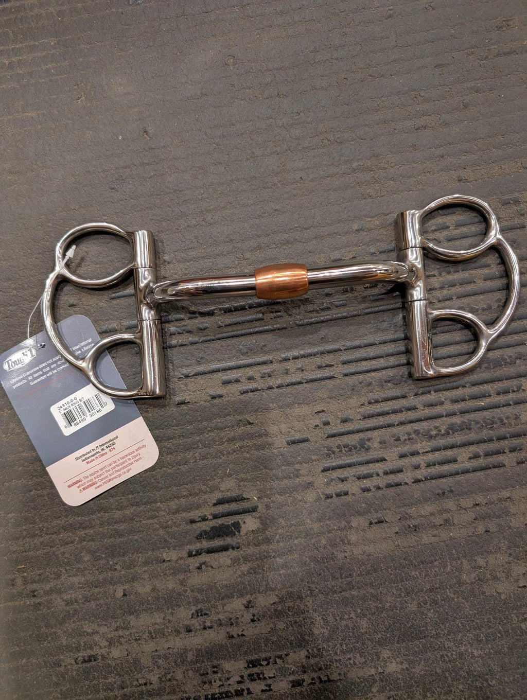 Metal horse bridle bit on a textured surface with a visible brand tag.
