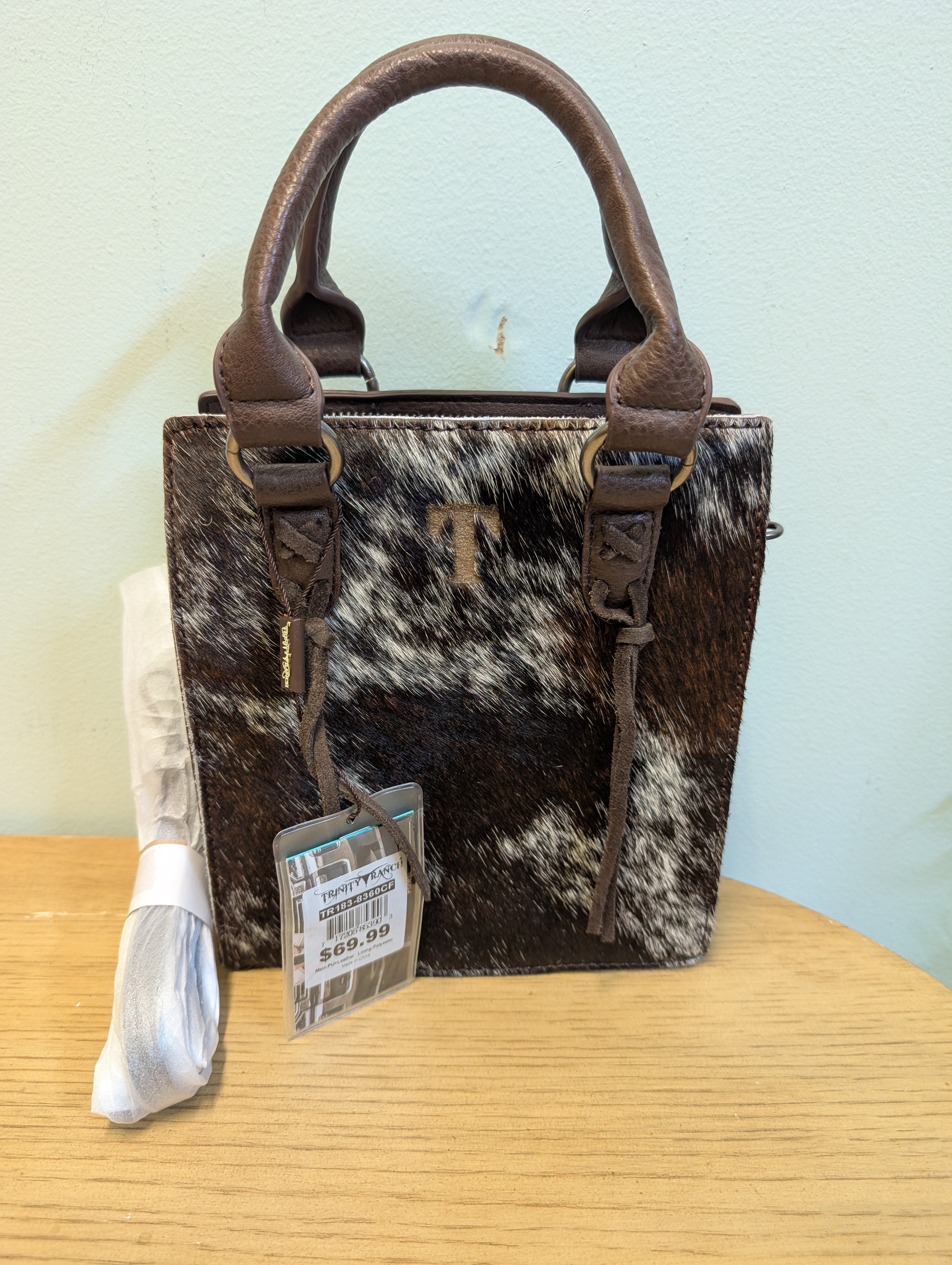 Handbag with cowhide pattern and brown handles on a wooden surface