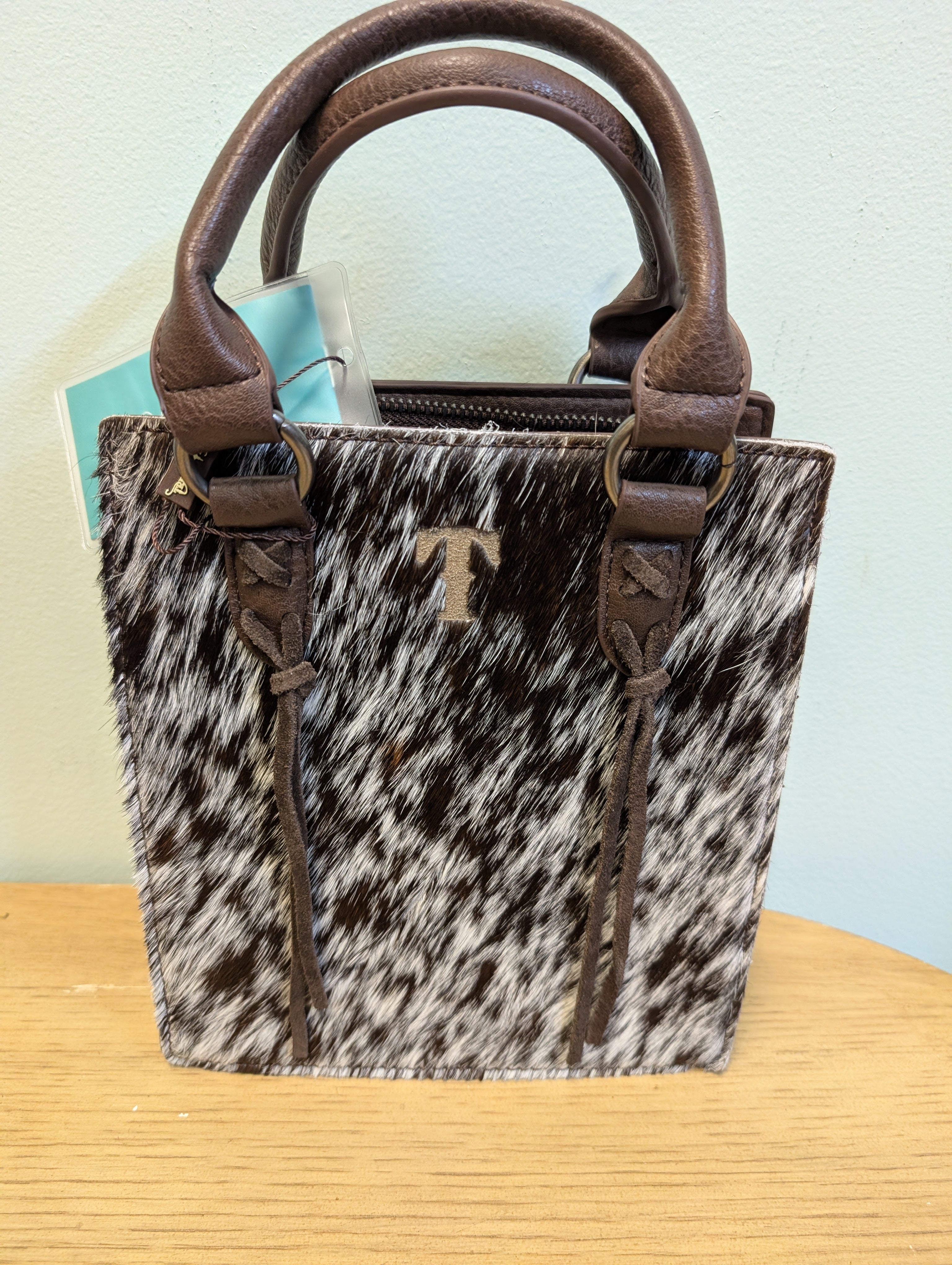 Handbag with cow print pattern and brown handles on a wooden surface