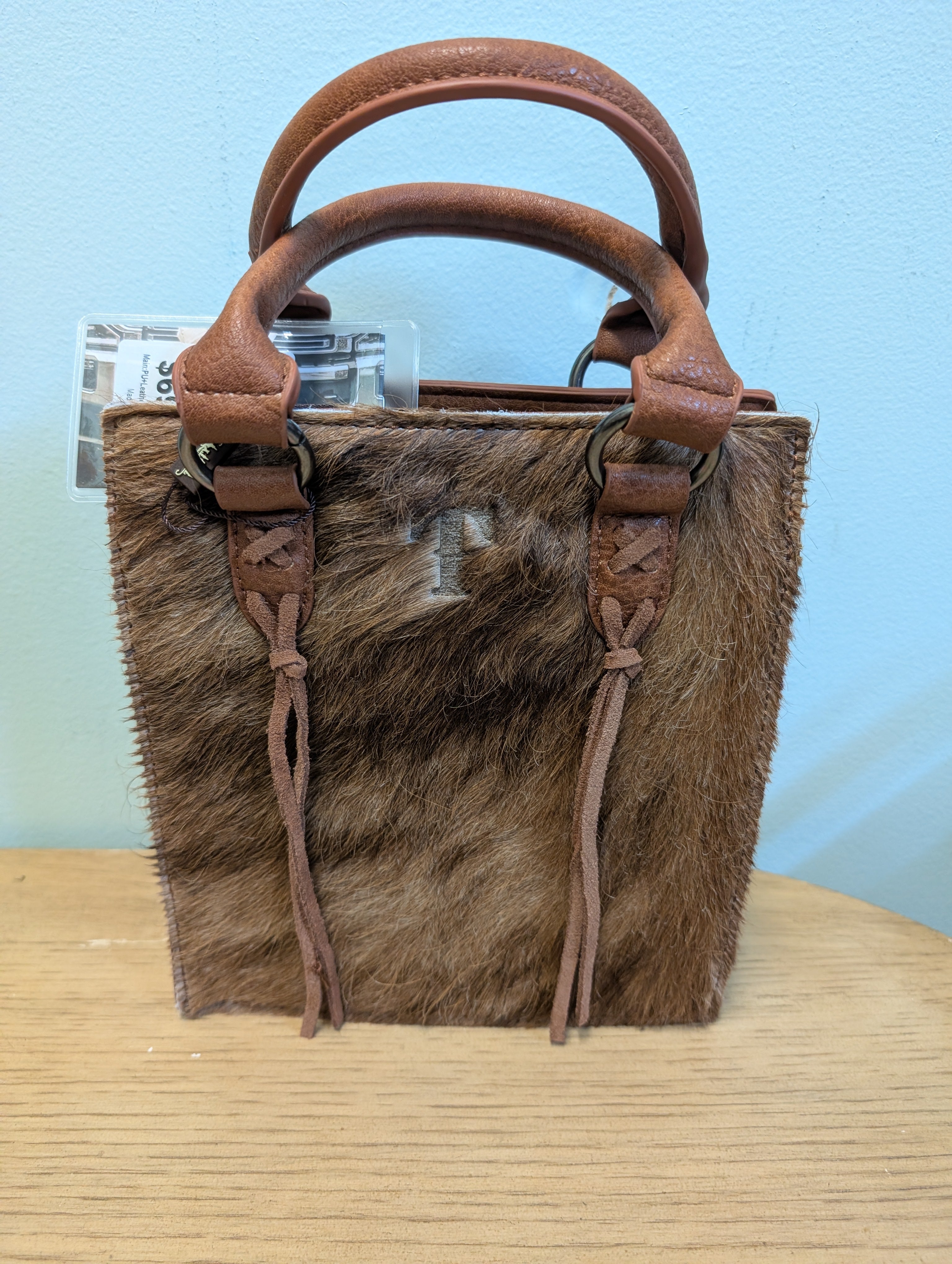 Brown fur handbag with leather handles and straps on a light blue background