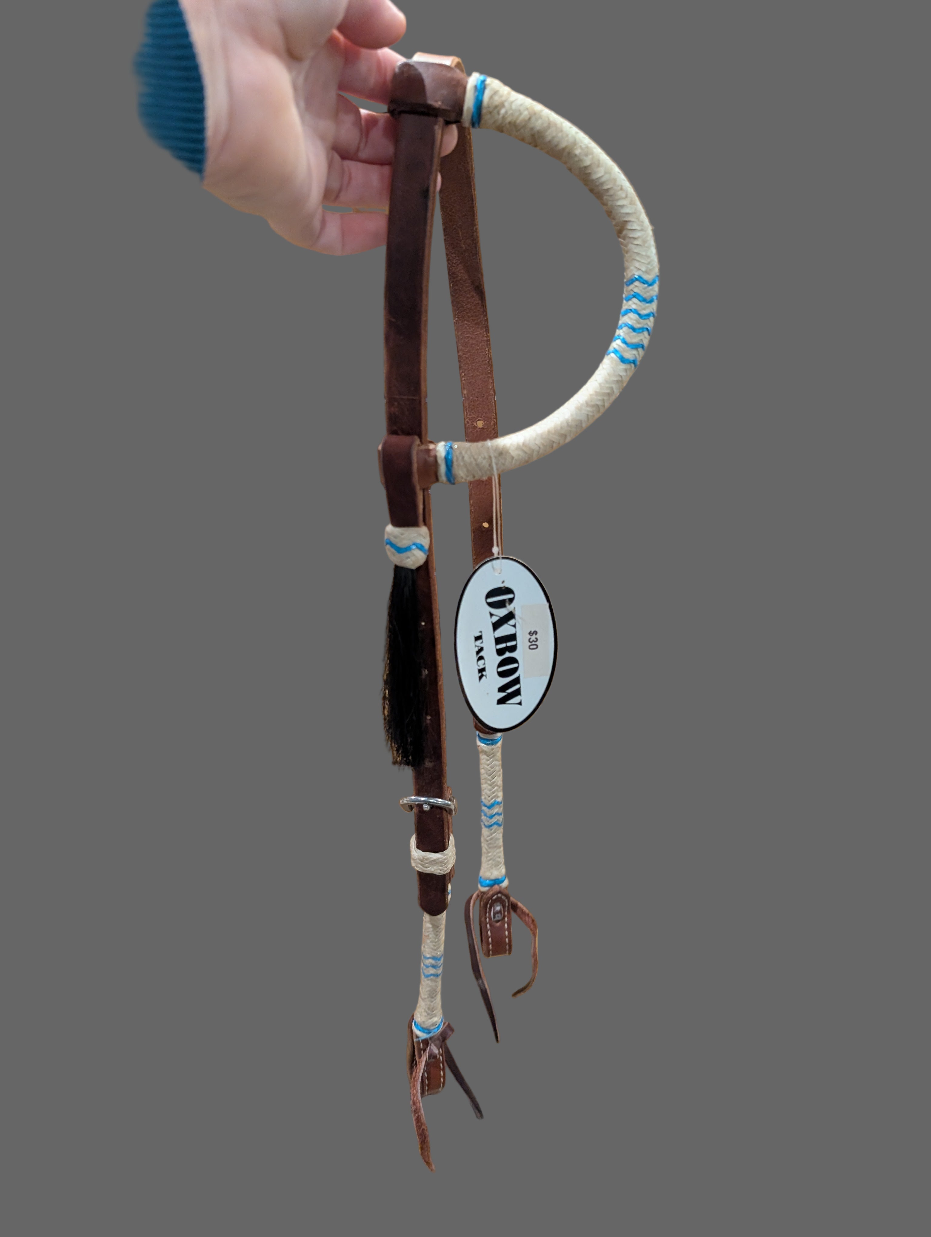 Horse bridle with leather and rope details held by a person against a wooden background