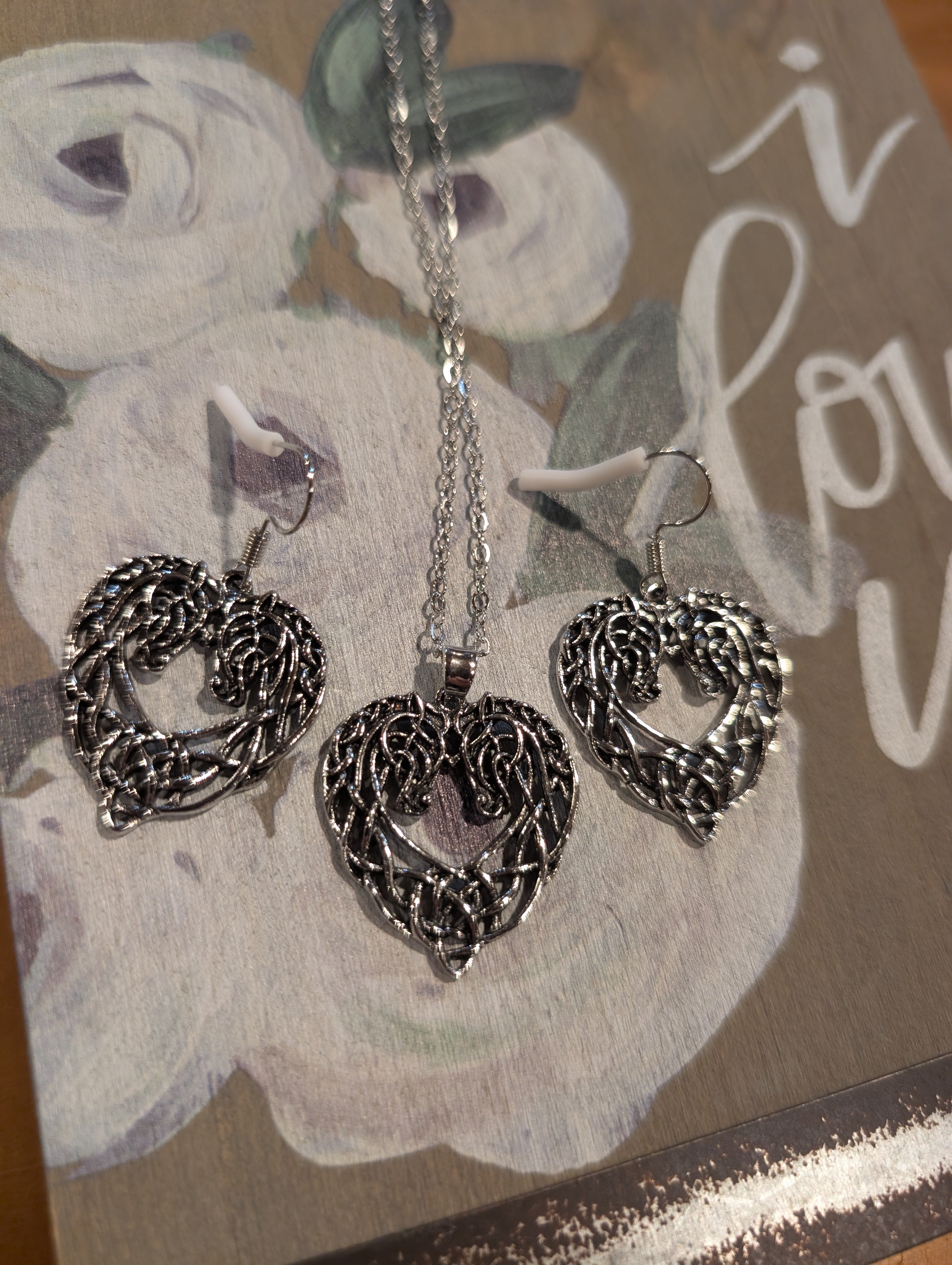 Silver heart-shaped necklace and earrings on a floral card