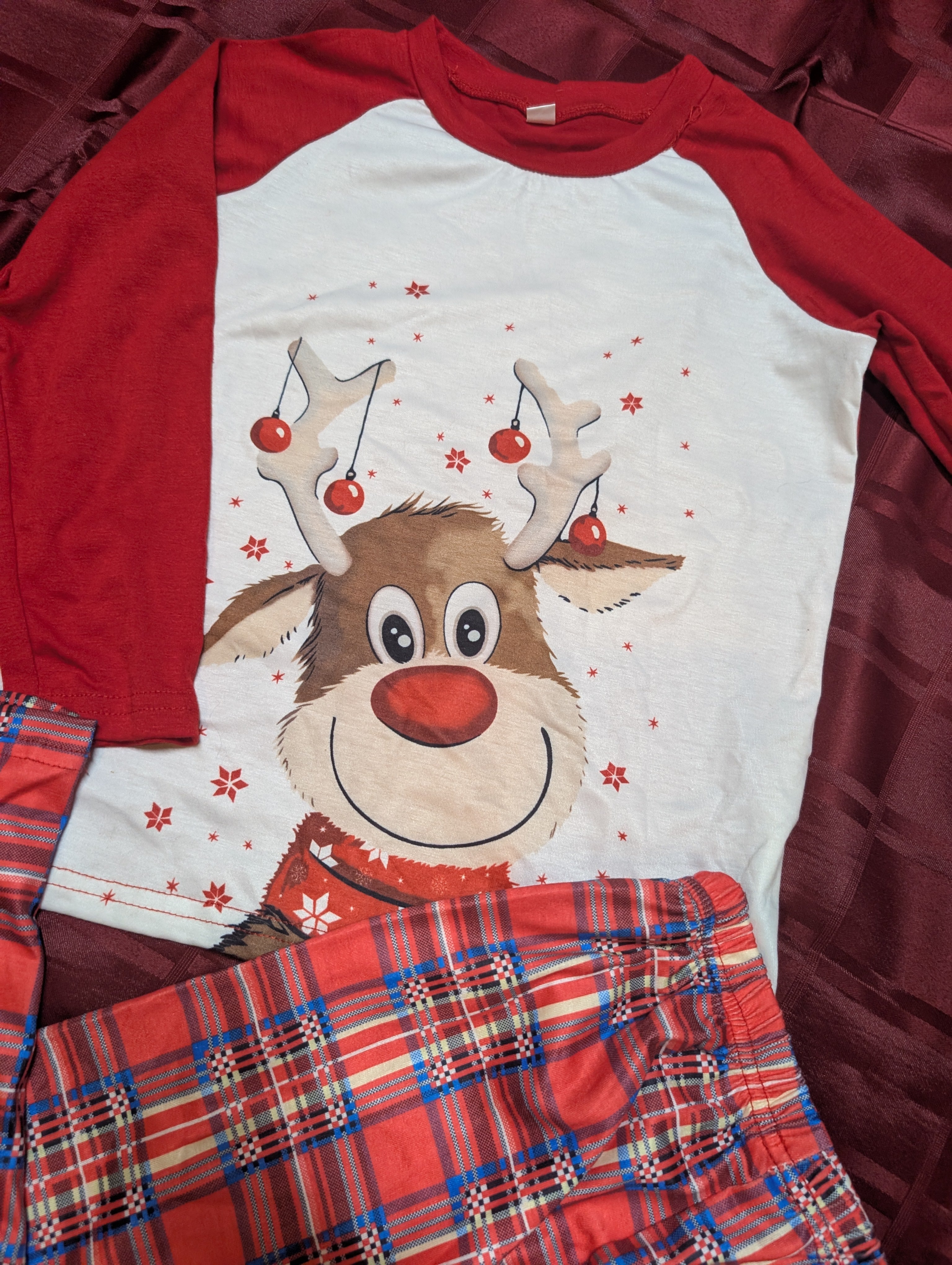 Red and white long-sleeve shirt with a reindeer design on a red plaid fabric background.