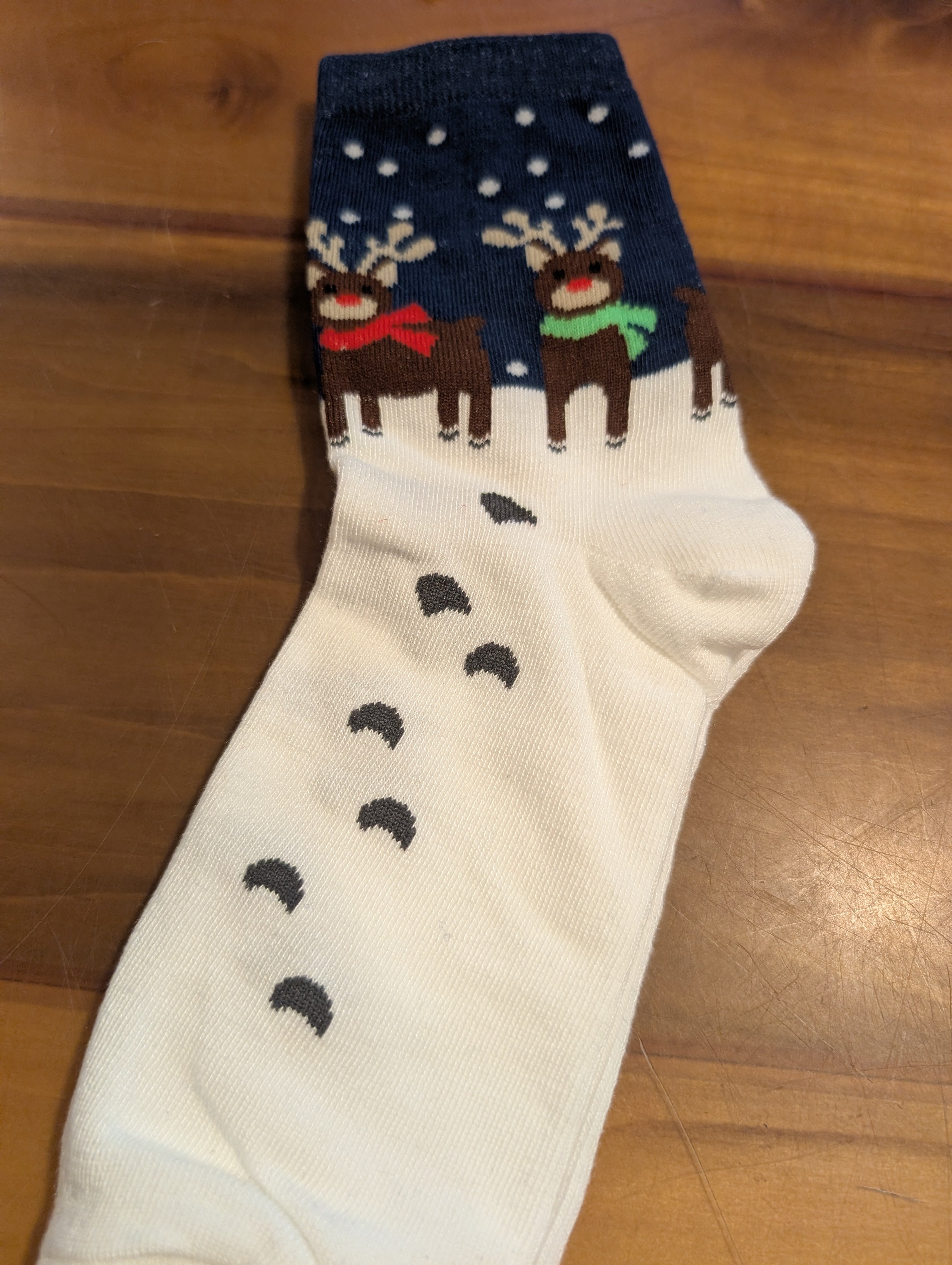 Christmas-themed sock with reindeer and snowflakes on a wooden floor