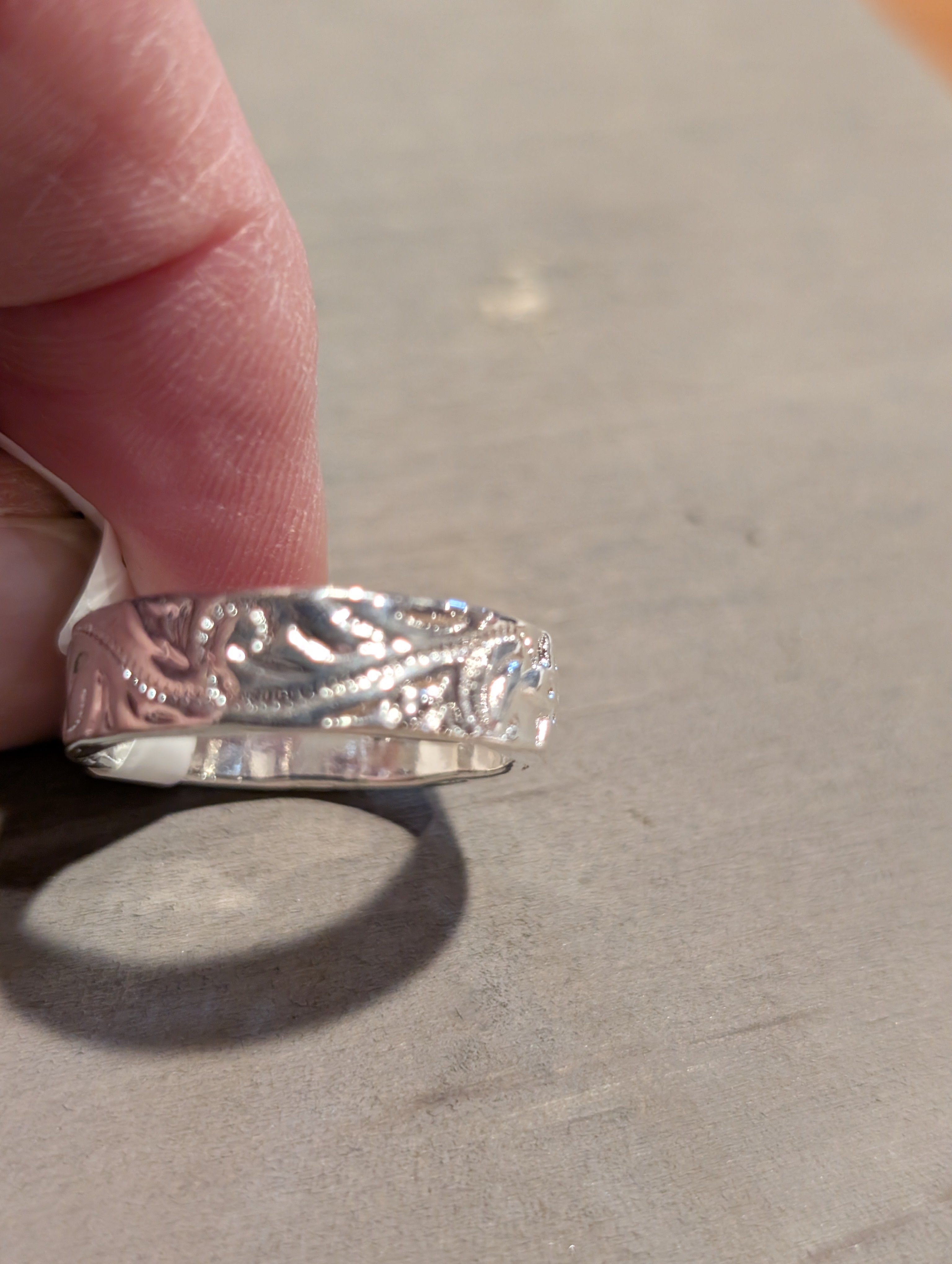 Silver ring with intricate design held by a finger on a neutral background
