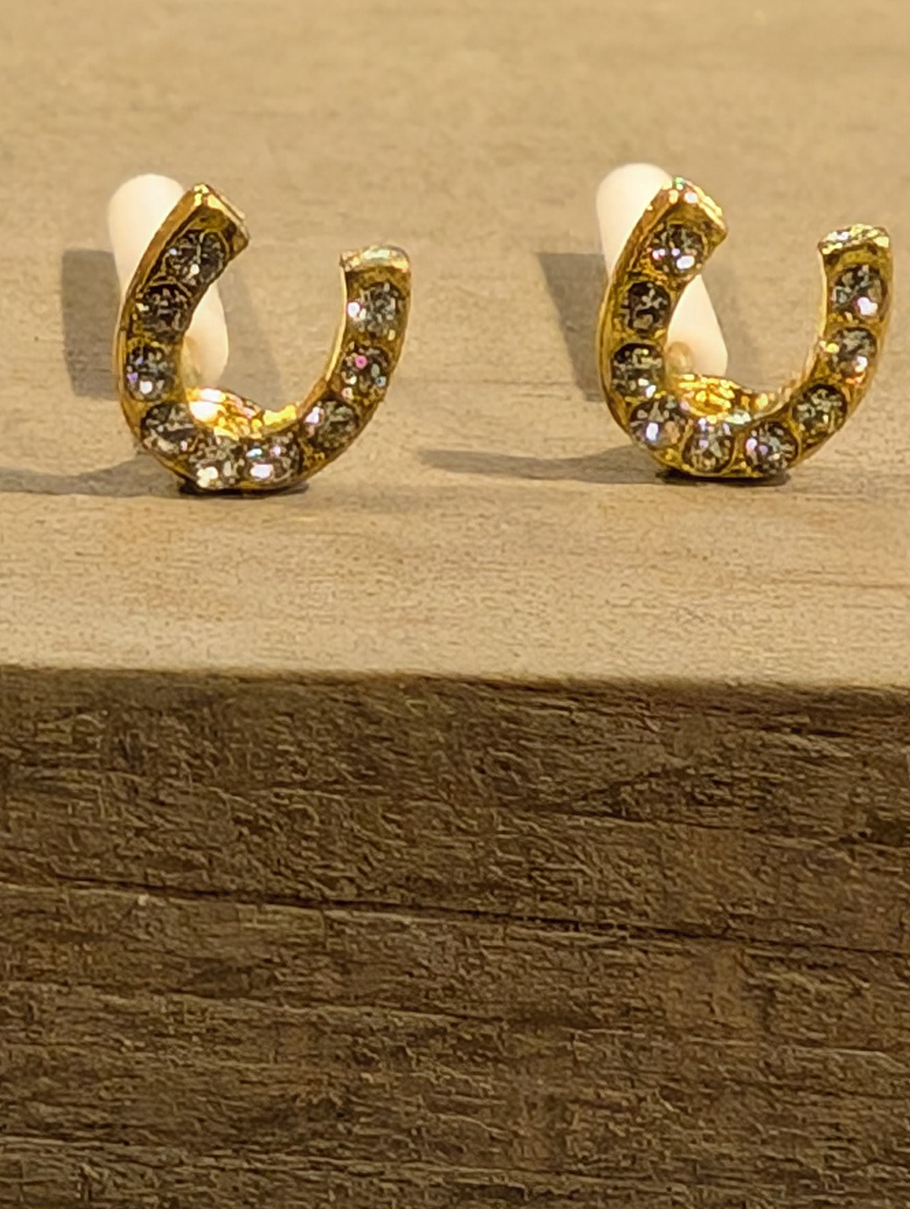 Gold horseshoe-shaped earrings with rhinestones on a wooden surface