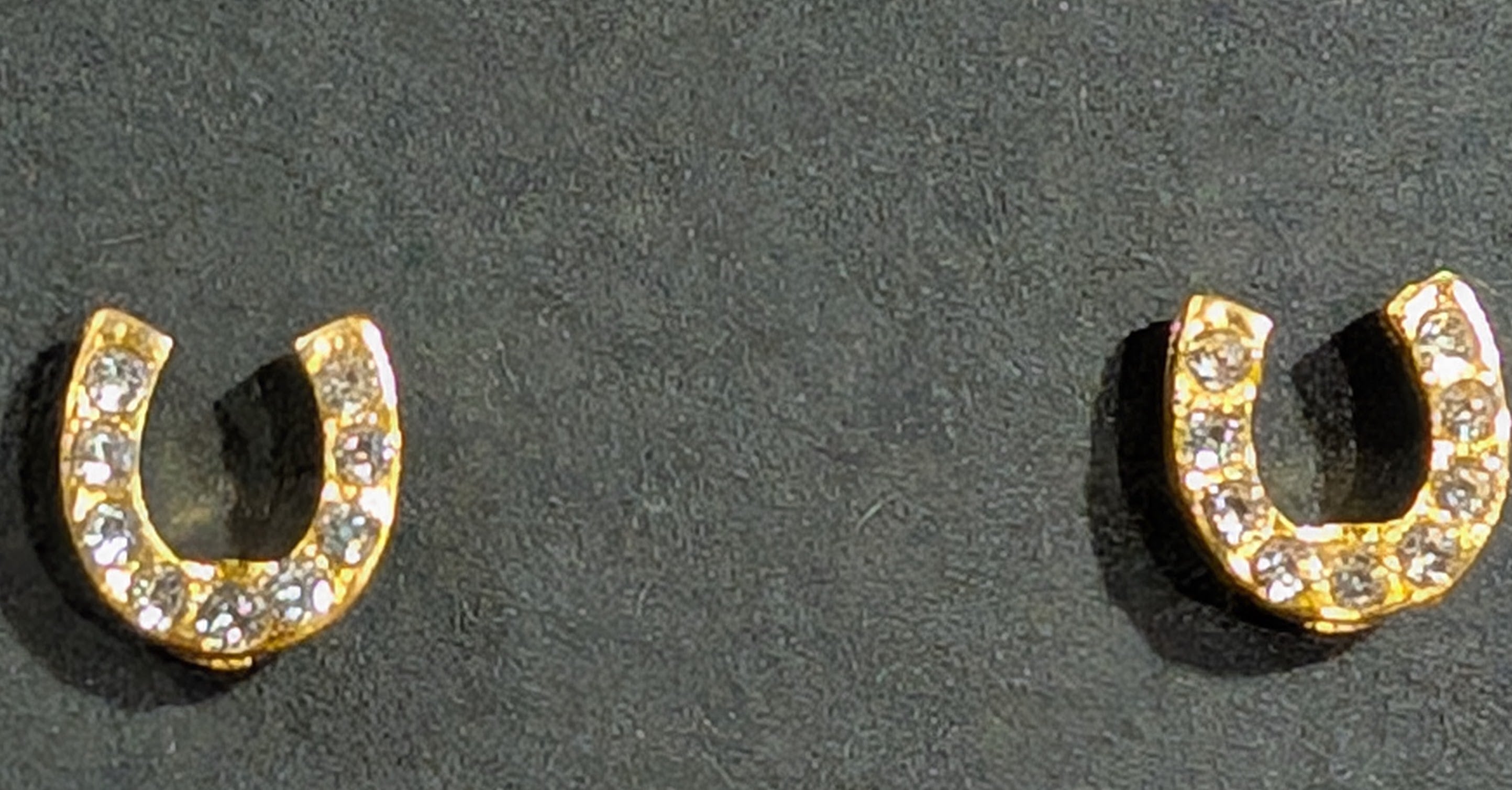 Gold horseshoe-shaped earrings with embedded stones on a dark background
