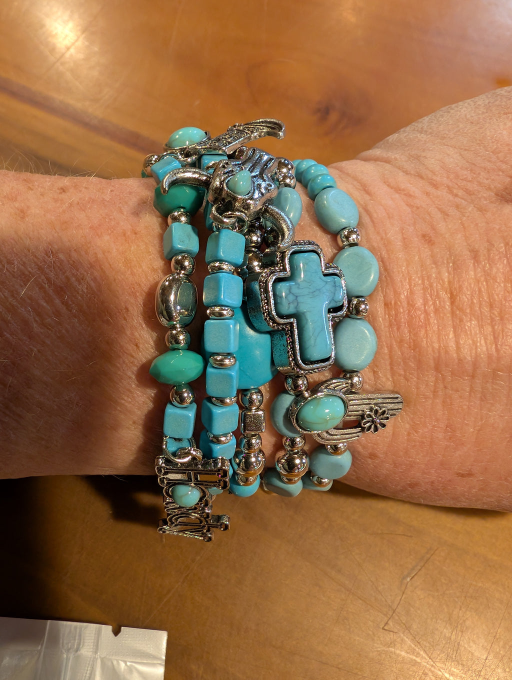 Turquoise beaded bracelet with silver charms on a wrist against a wooden background