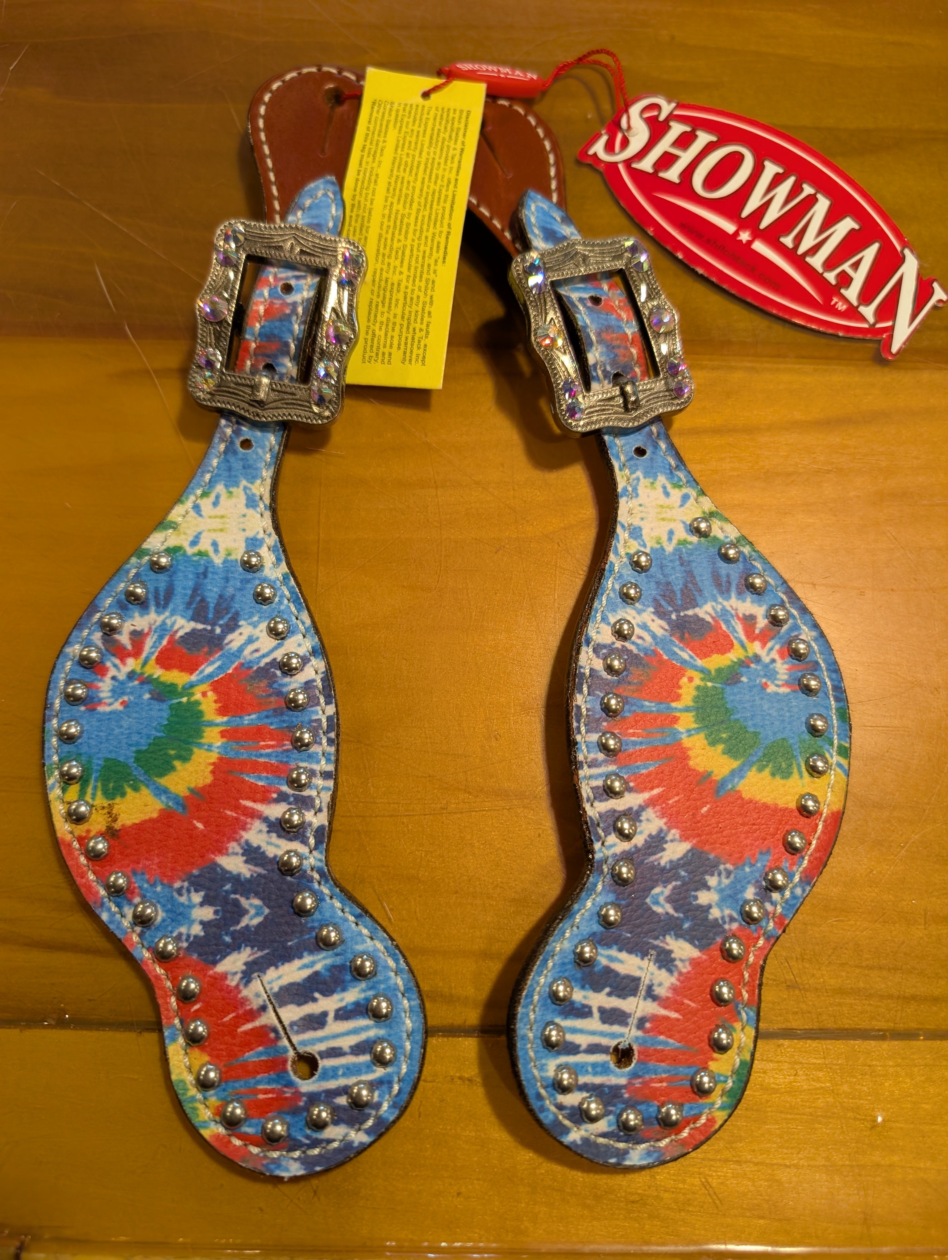 Colorful tie-dye spurs with decorative elements on a wooden surface, featuring a 'Showman' brand tag.