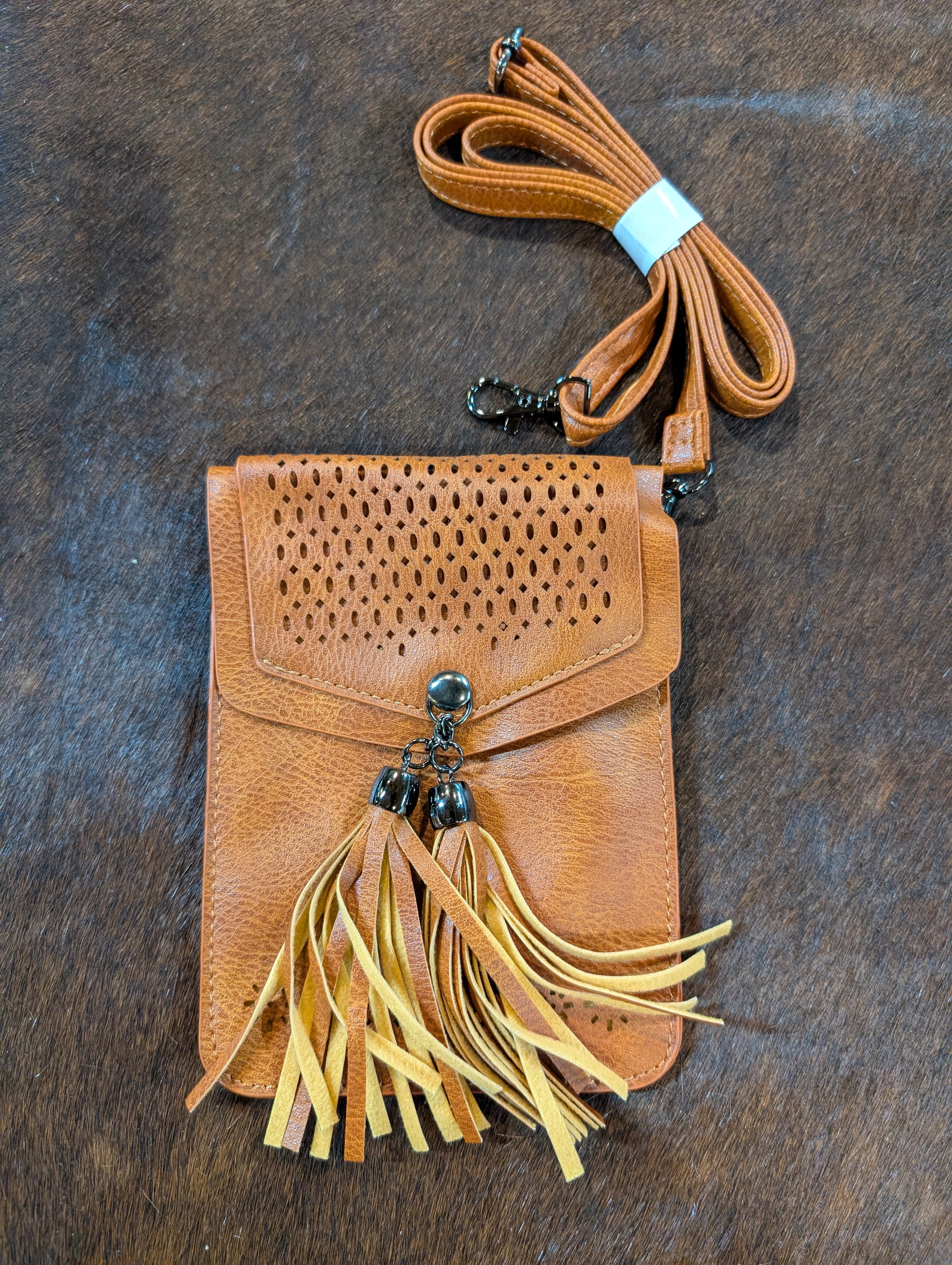 Brown leather crossbody bag with fringes on a dark brown surface