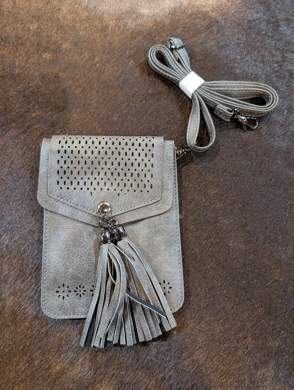 Gray suede crossbody bag with perforated design and tassel on a brown surface
