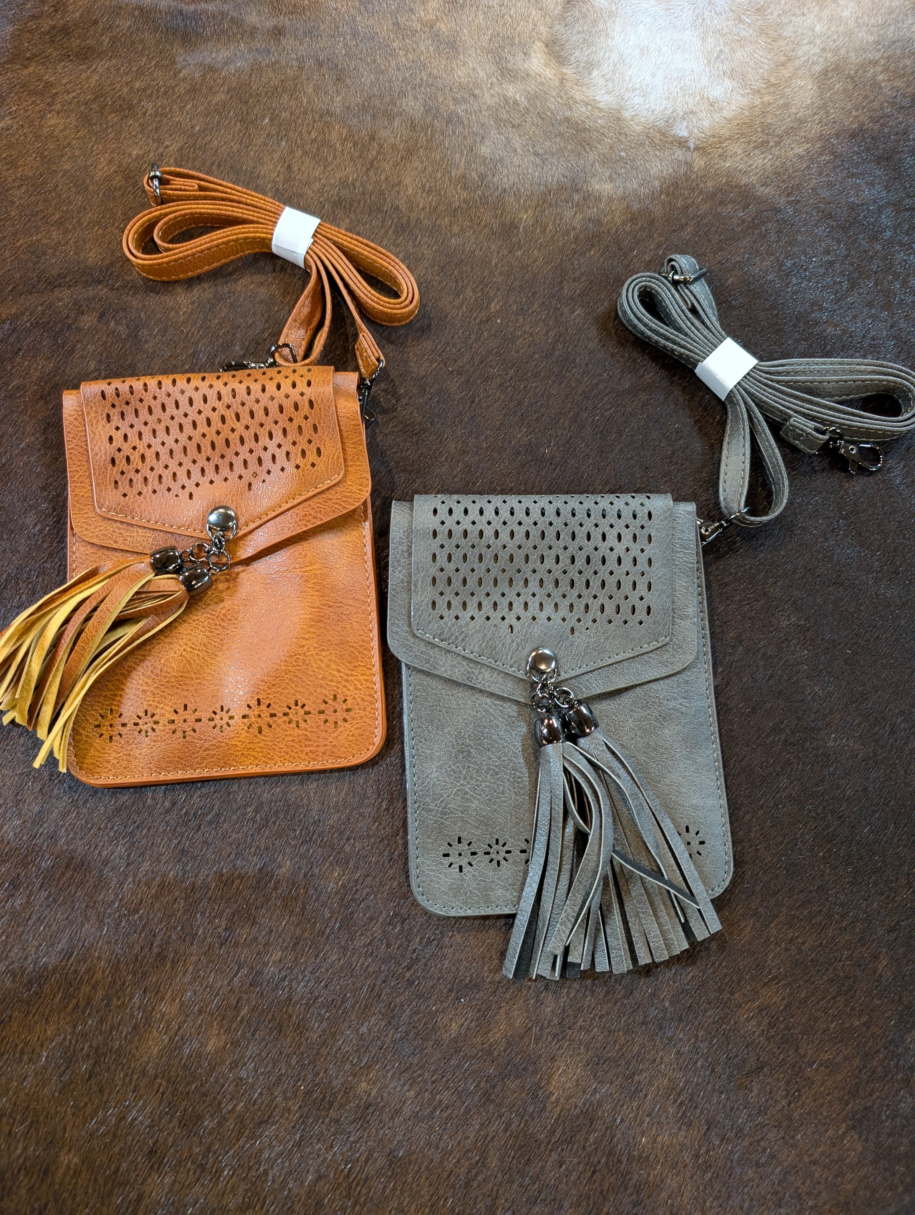 Two small handbags, one brown and one gray, with tassels on a textured surface.