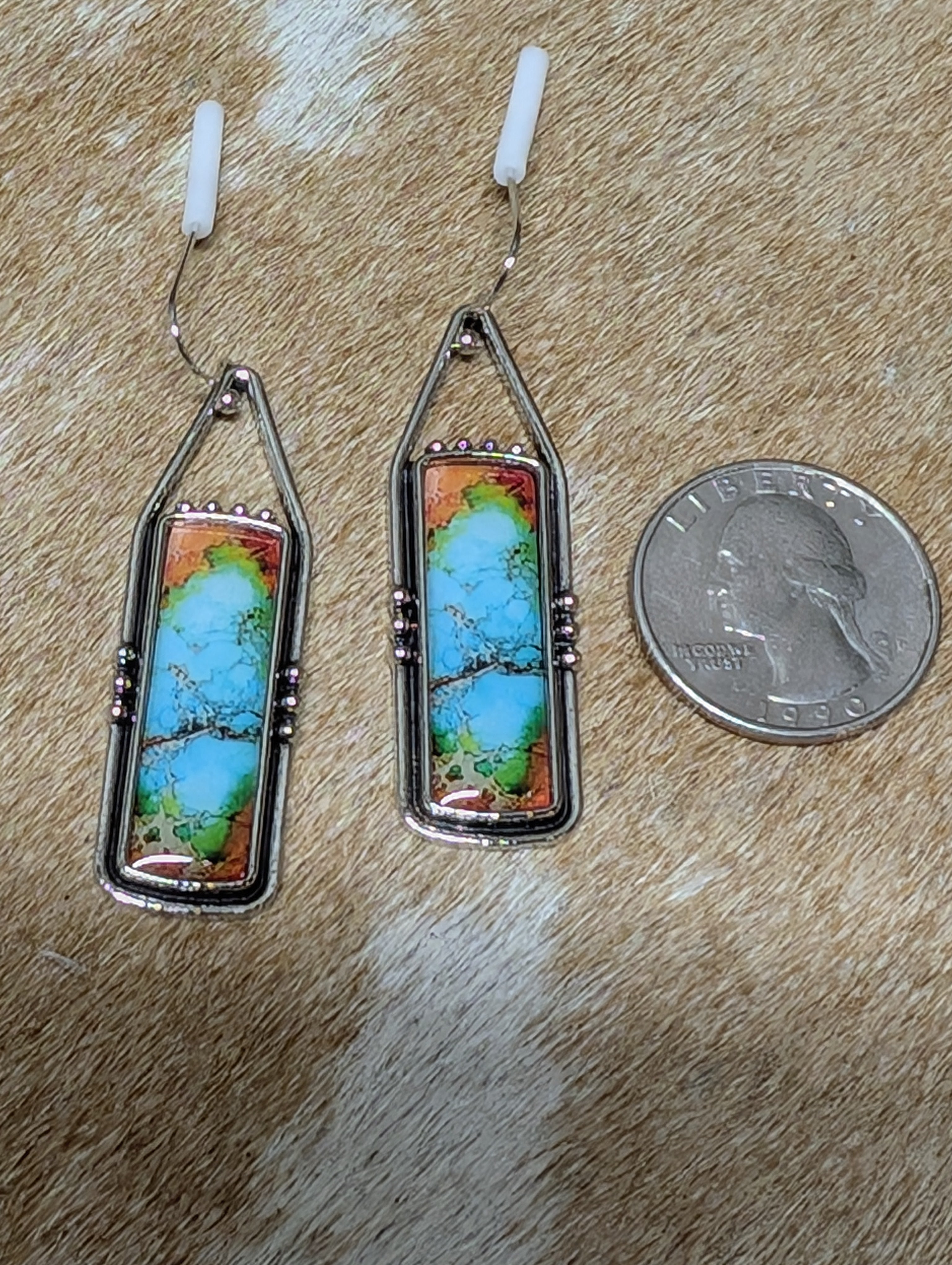 Pair of earrings with a natural stone design on a wooden surface next to a penny for scale.