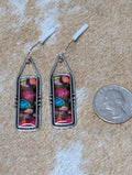 Pair of colorful earrings with floral design on a wooden surface next to a quarter for scale.