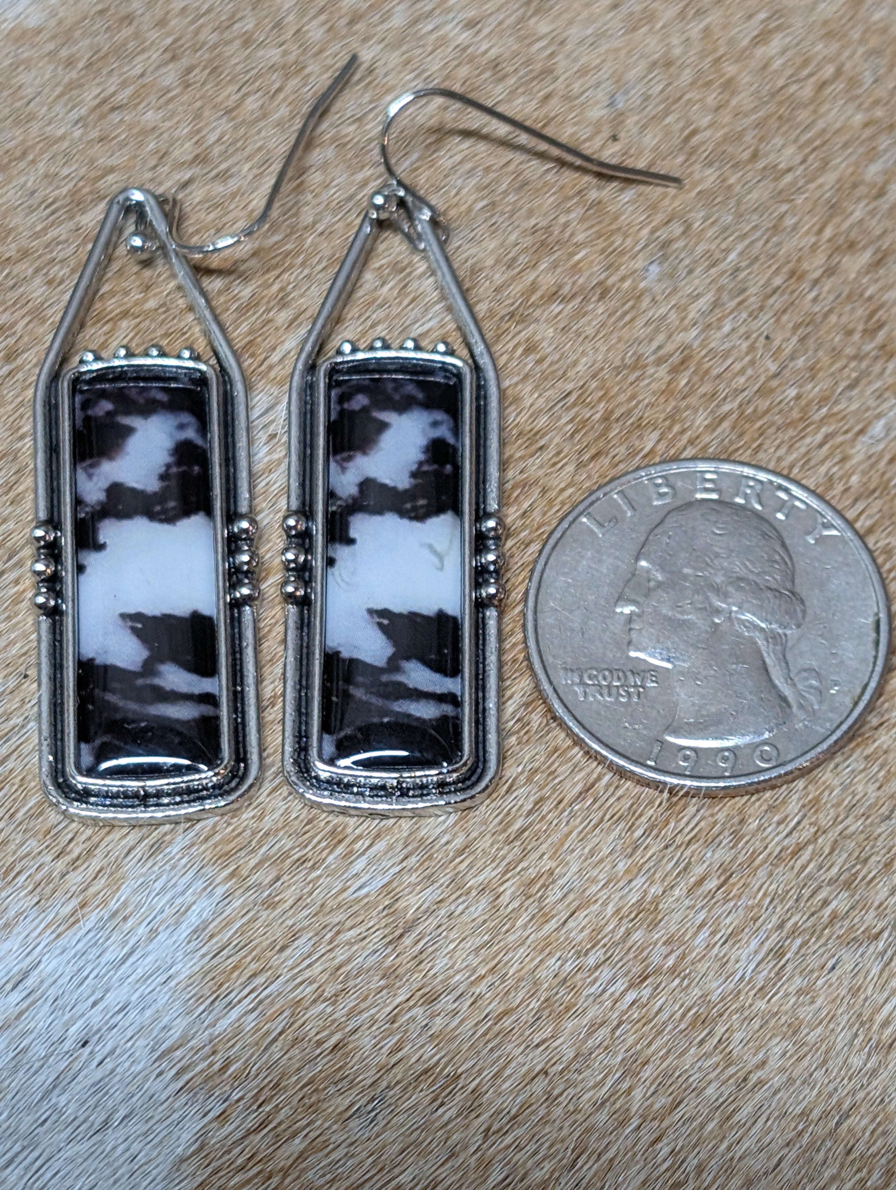 Pair of silver-framed earrings with black and white marbled design, next to a quarter for scale on a wooden surface.