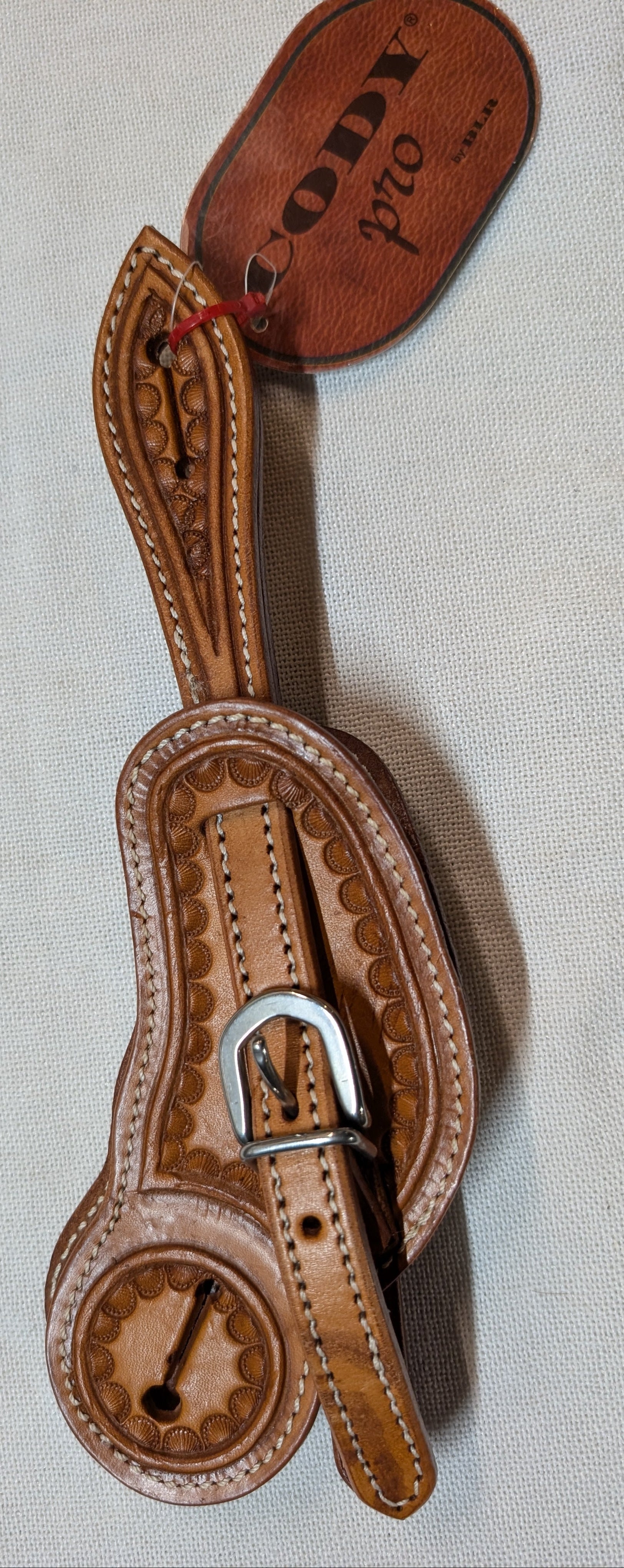 Brown leather spur with intricate designs on a light gray background