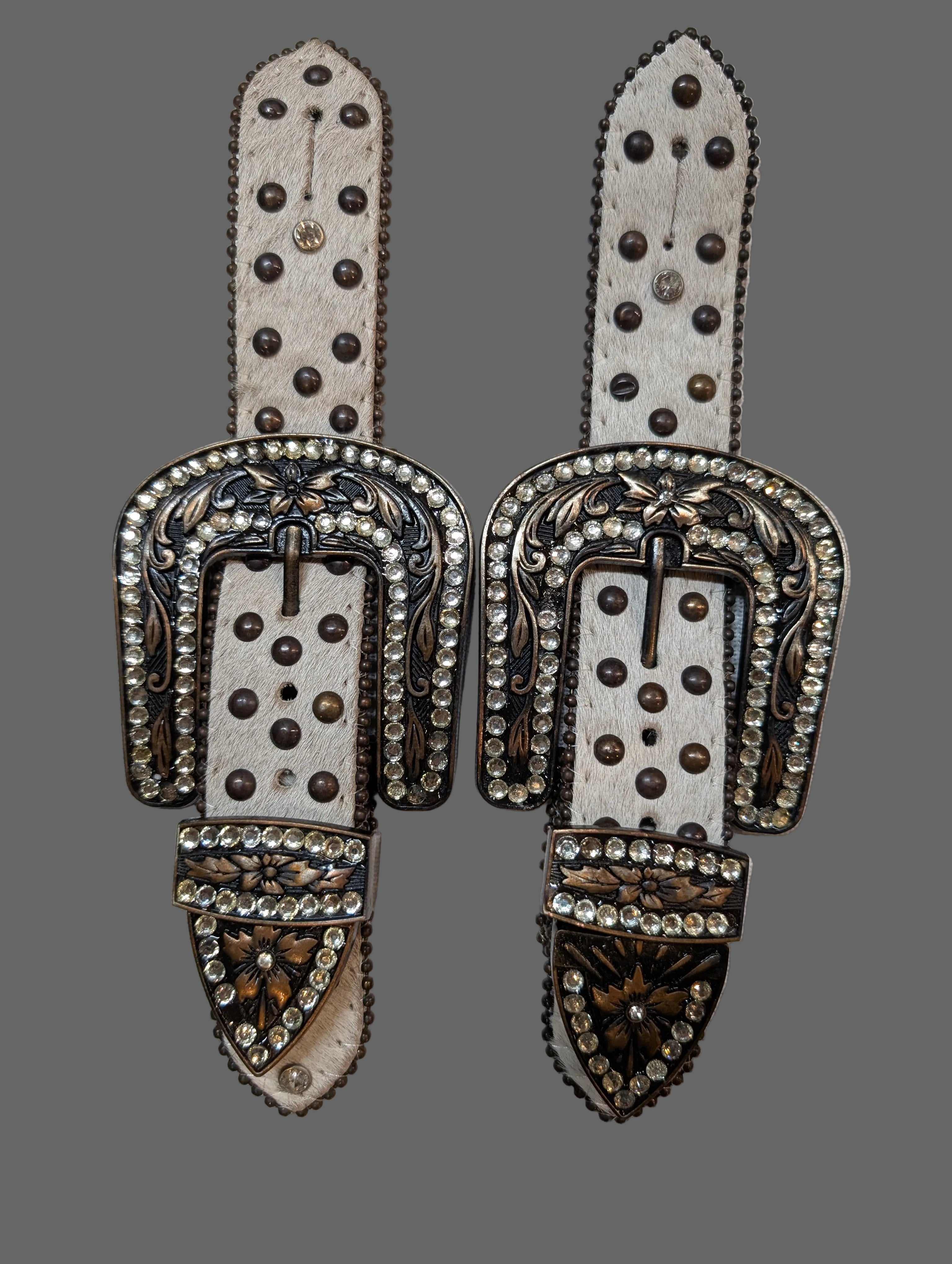 Decorative leather spur straps with metal embellishments on a white background