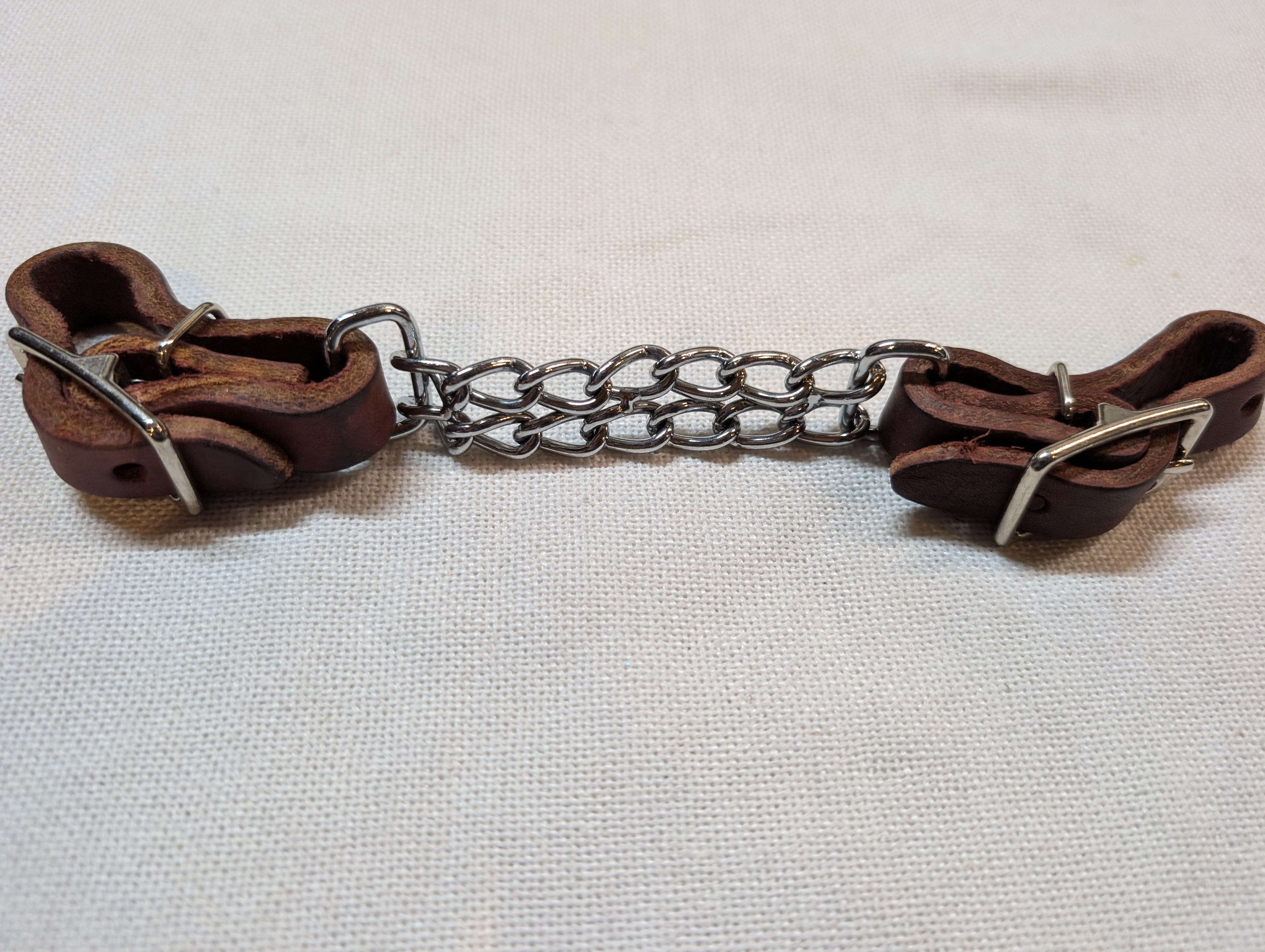 Brown leather bridle with metal chain on a light fabric background