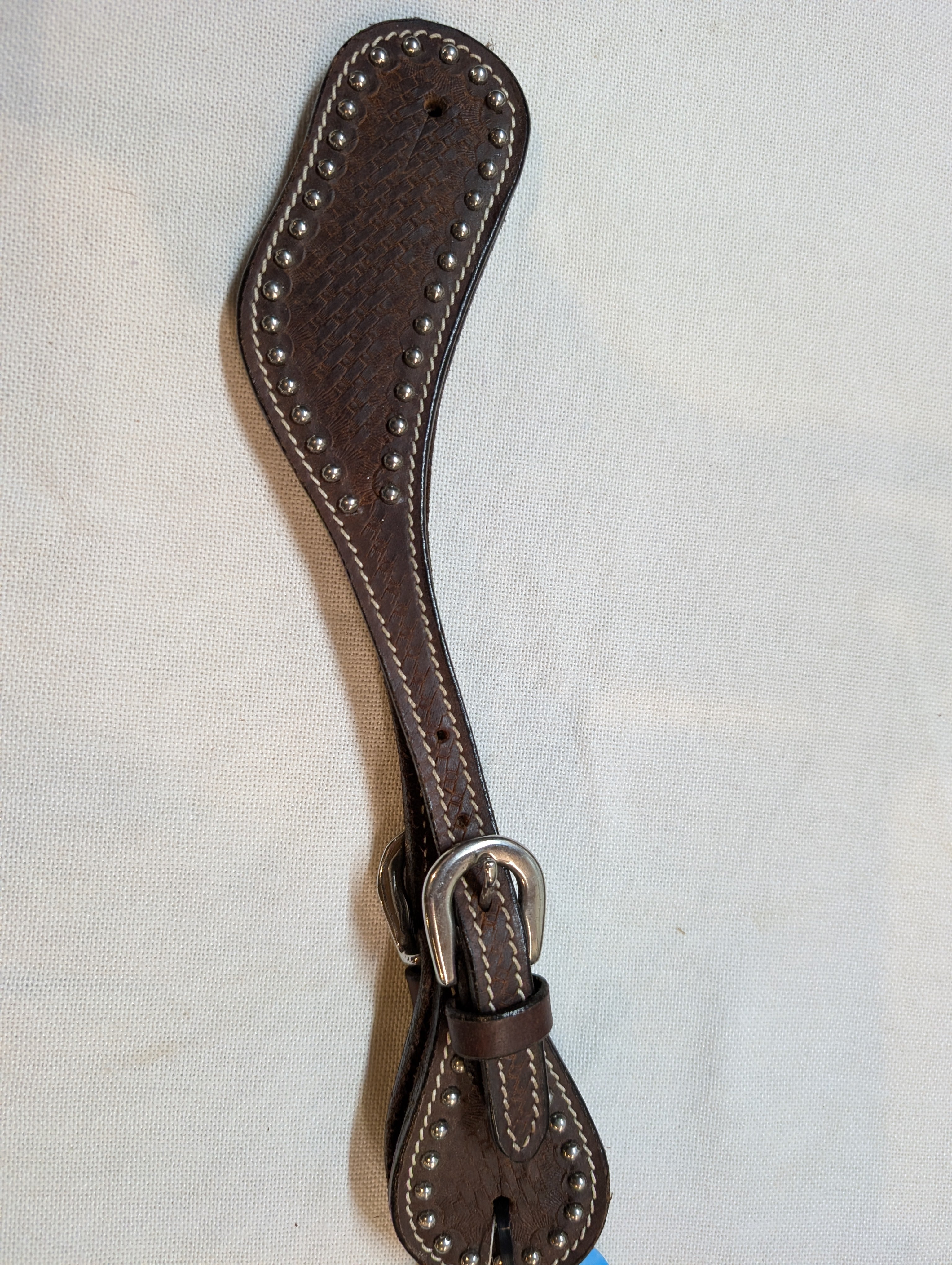 Brown leather spur strap with a silver buckle on a light beige background