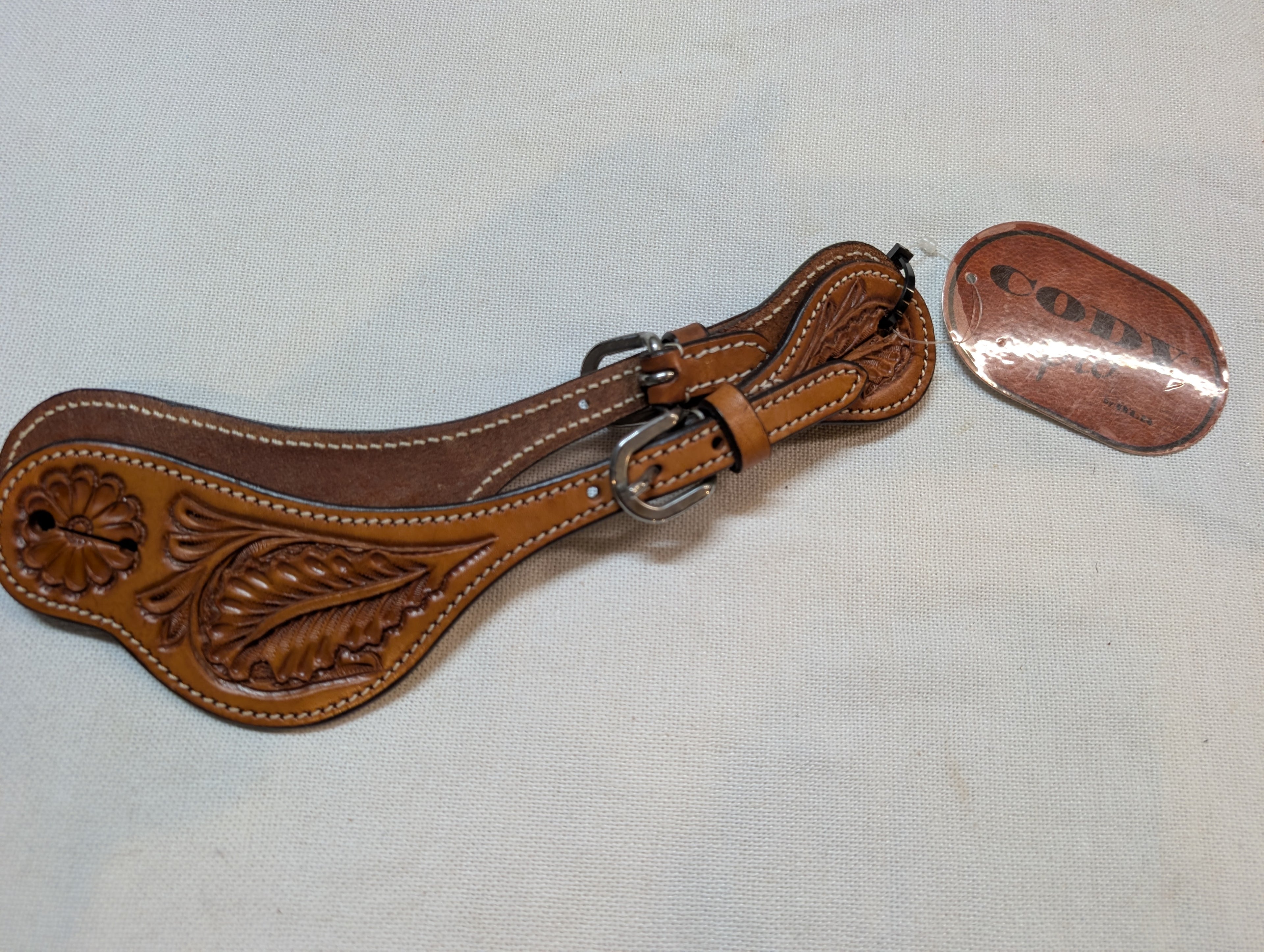 Brown leather spur with decorative patterns on a light gray background