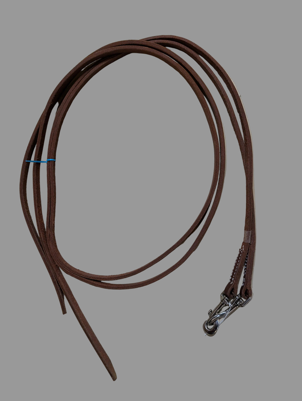 Brown leather split reins with a metal clasp on a light-colored floor.