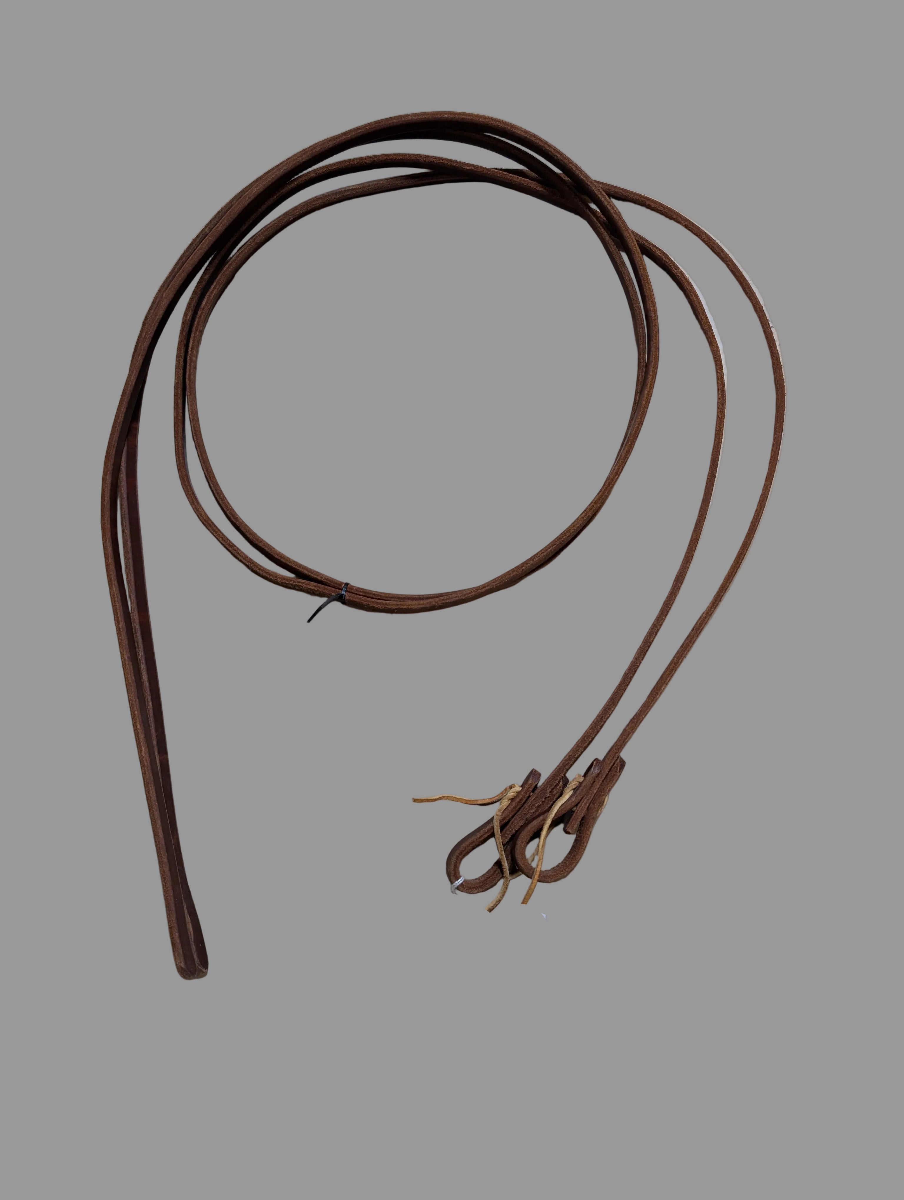 Brown leather split reins on a grey surface