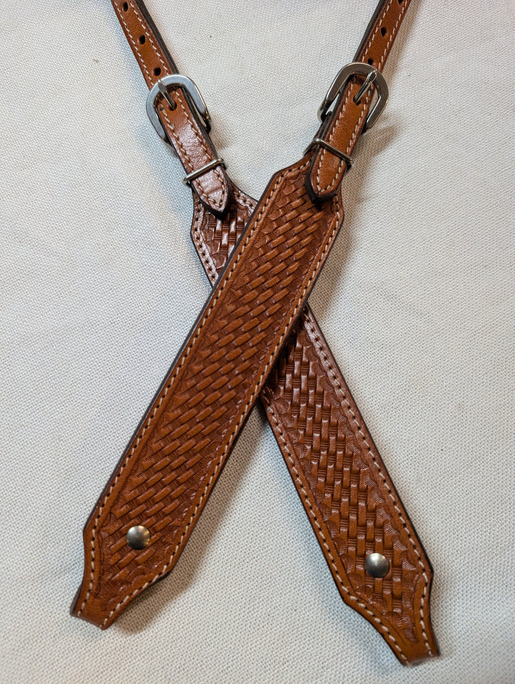 Brown leather straps with woven pattern and metal buckles on a light gray background