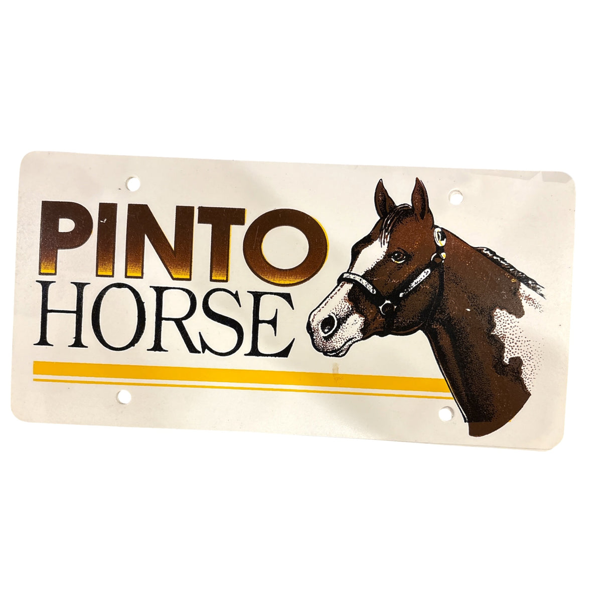 A vintage-style plastic licence plate  featuring the words 'PINTO HORSE' with a painted brown horse head on the right. The plate has gold and black lettering, and two yellow horizontal stripes near the bottom, with mounting holes visible.