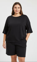 Black short sleeve drop shoulder in a lady wearing shorts with a white background.