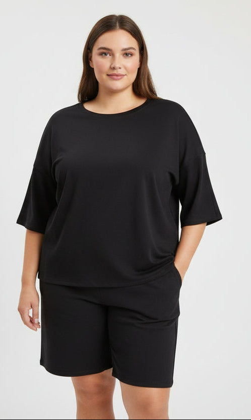 Black short sleeve drop shoulder in a lady wearing shorts with a white background.