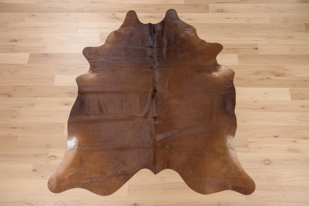 Reddish - Brown cowhide rug on a light wood floor.