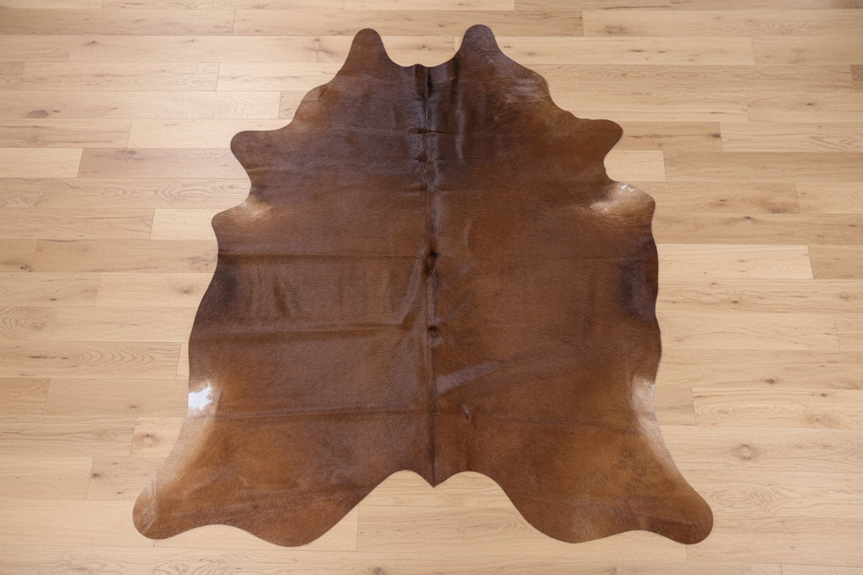 Reddish - Brown cowhide rug on a light wood floor.