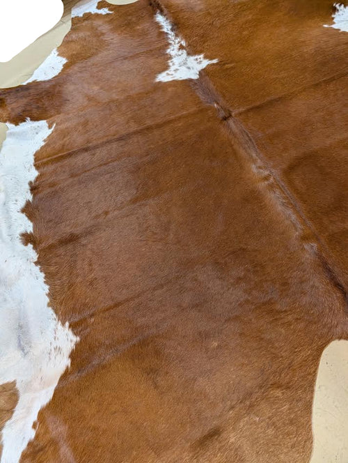 Brown and white cowhide rug on a beige floor