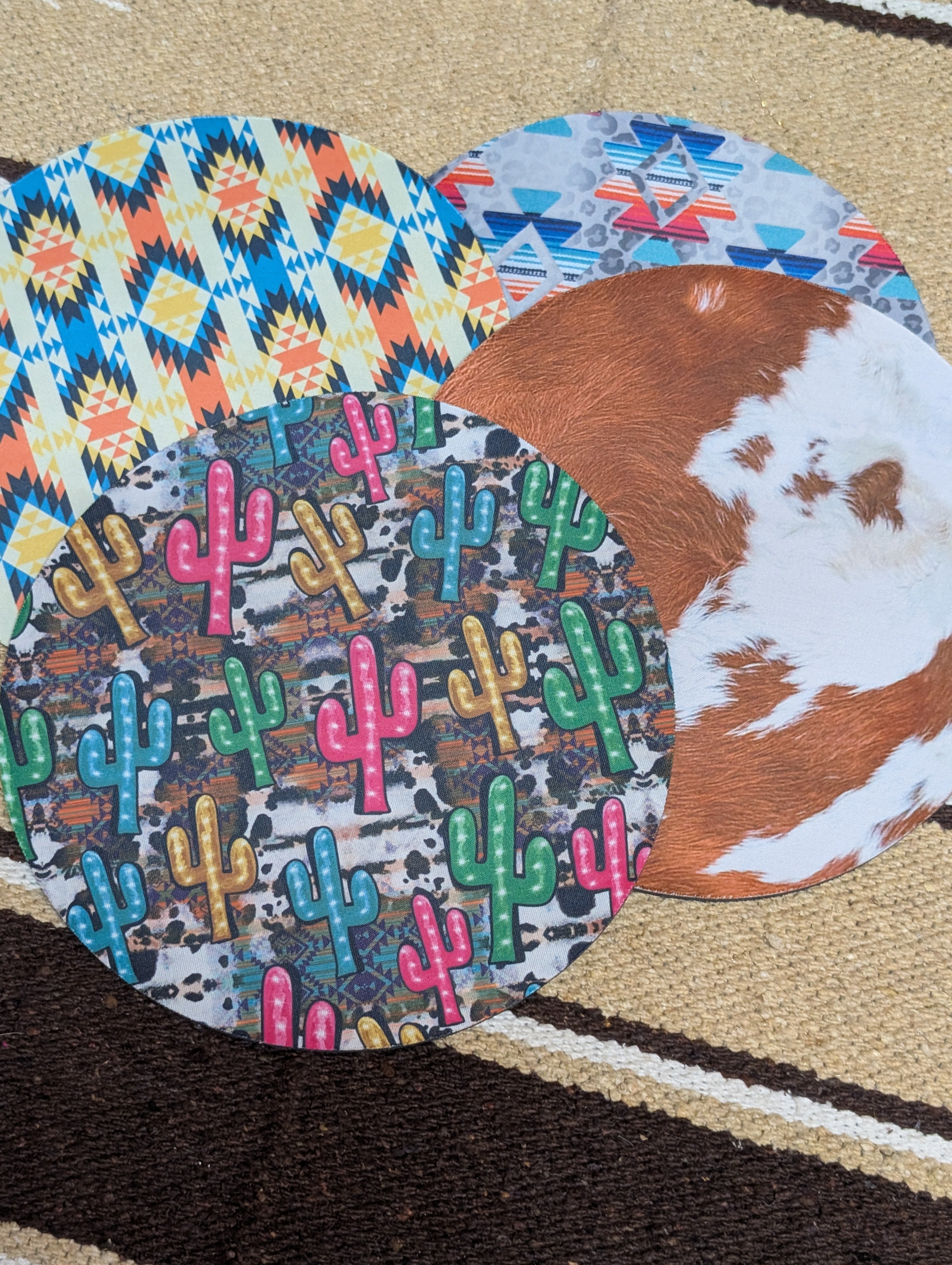 Colorful patterned coasters with cactus design and a cowhide coaster on a textured surface.