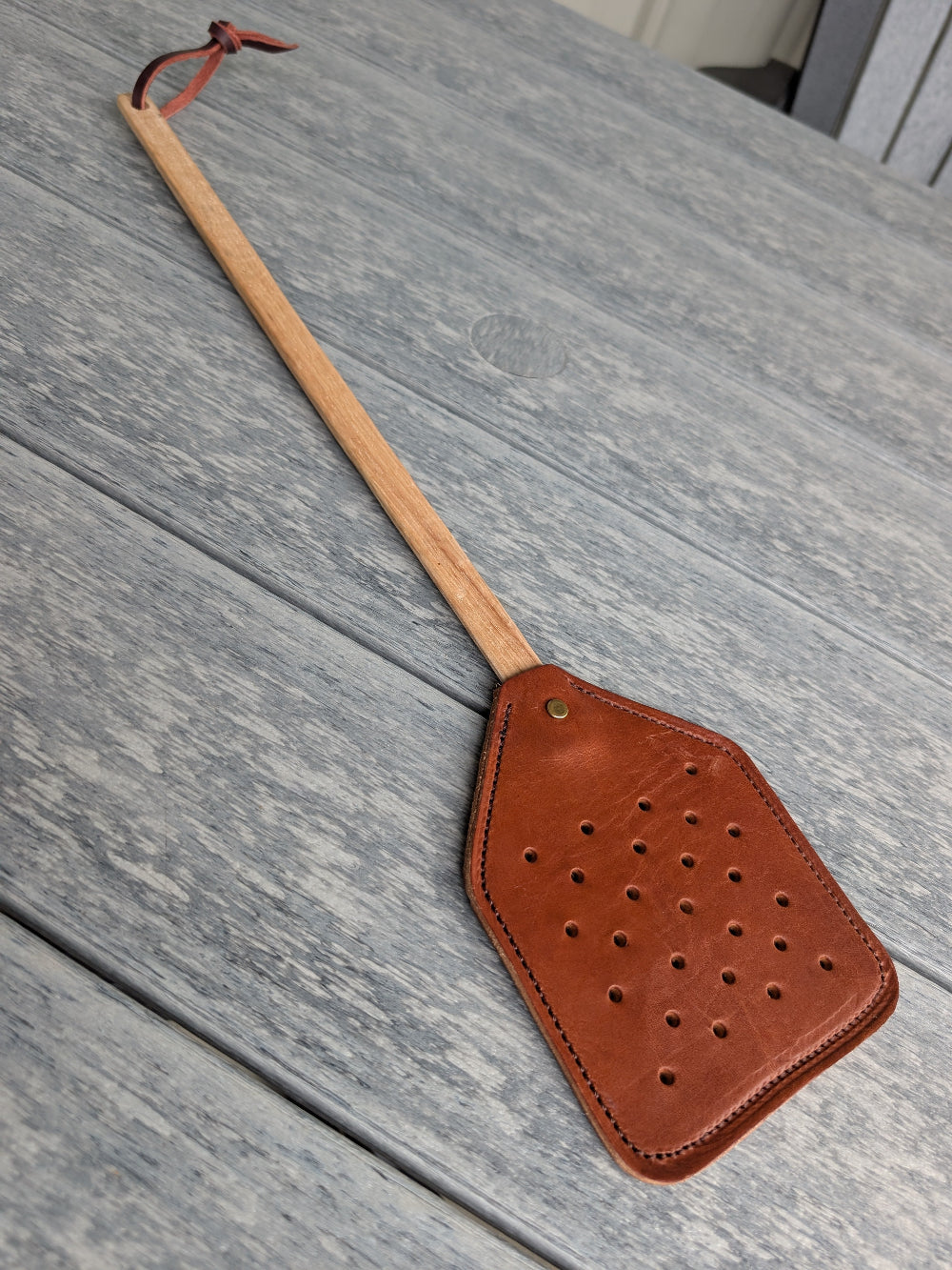 Rustic leather fly swatter with smooth wood handle for farmhouse or outdoor use