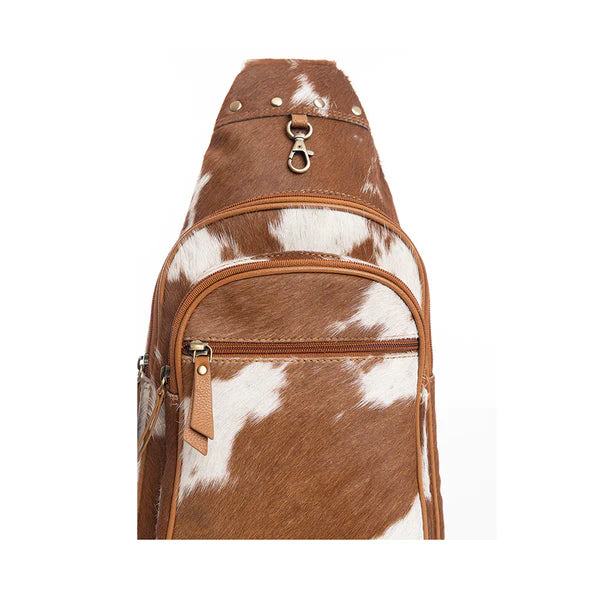 Brown and white cowhide patterned sling bag on a white background