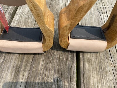 Two wooden stirrups with blackrubber bottoms on a wooden floor.