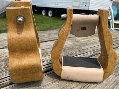 Wooden stirrups with leather straps on a wooden surface outdoors.