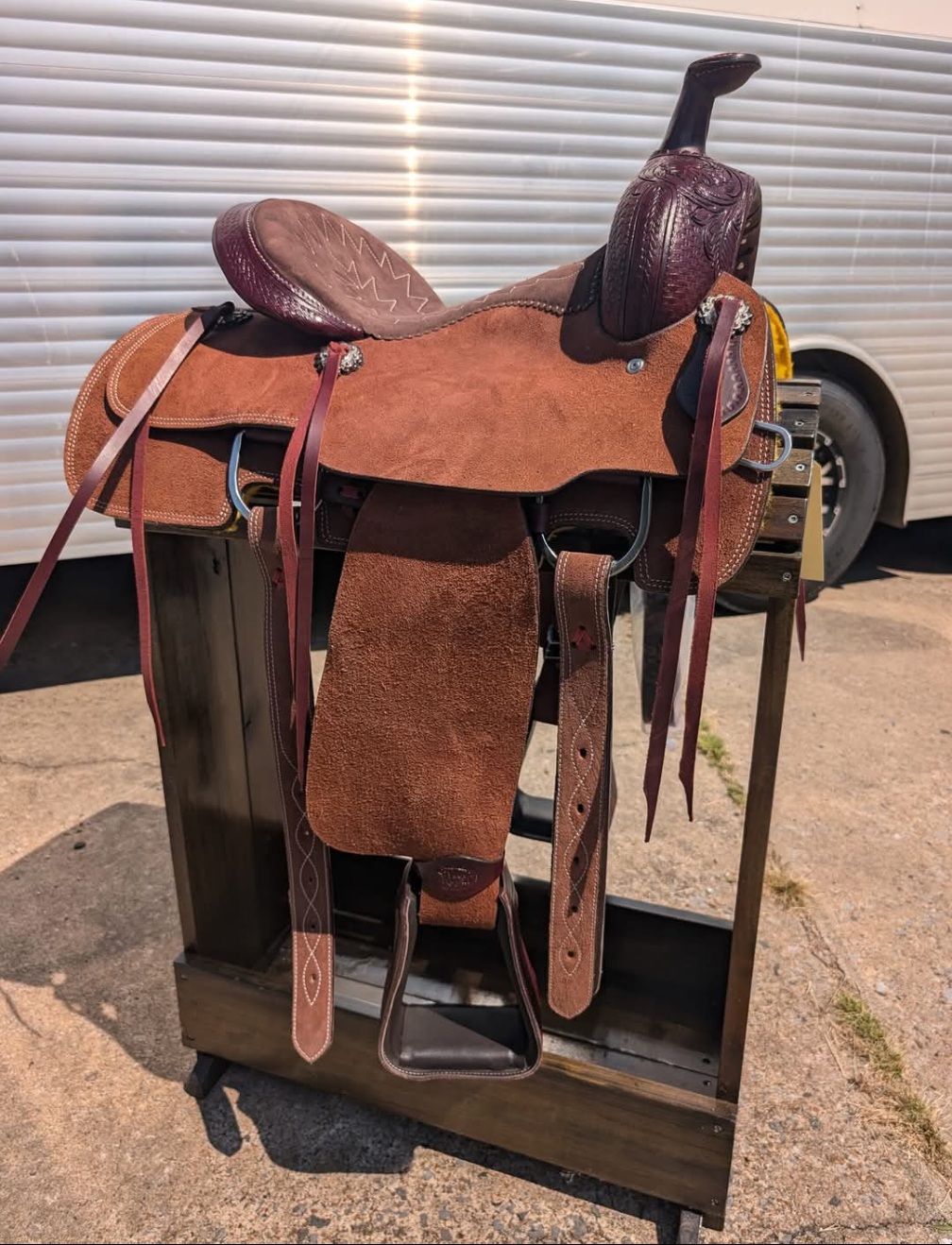 Brown leather saddle on a stand with a white vehicle in the background