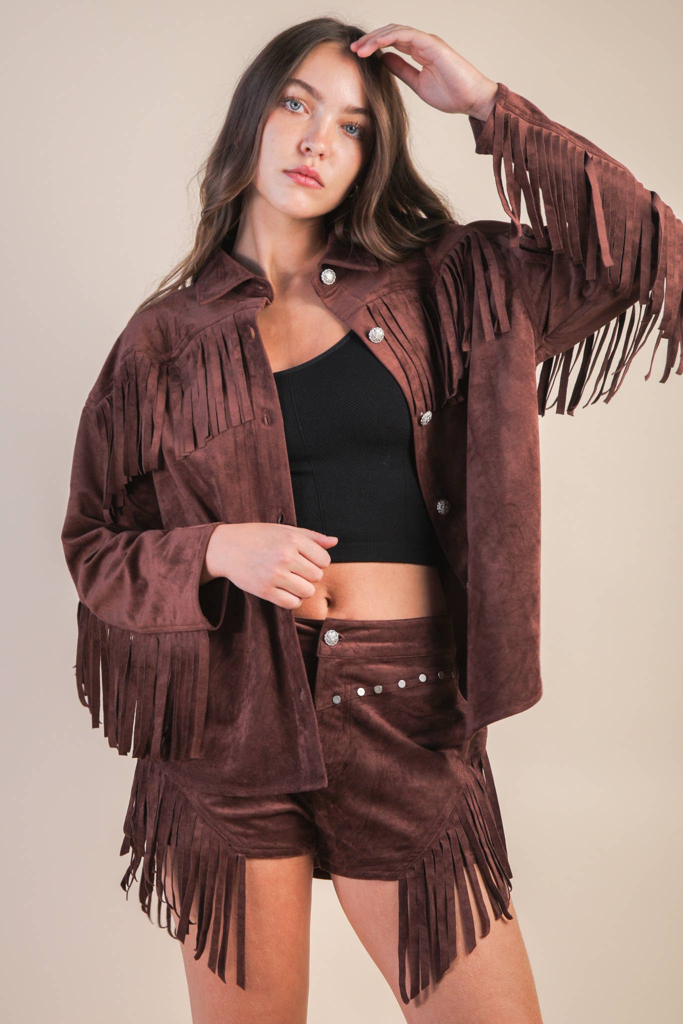 Woman wearing a brown suede fringe jacket and shorts on a beige background