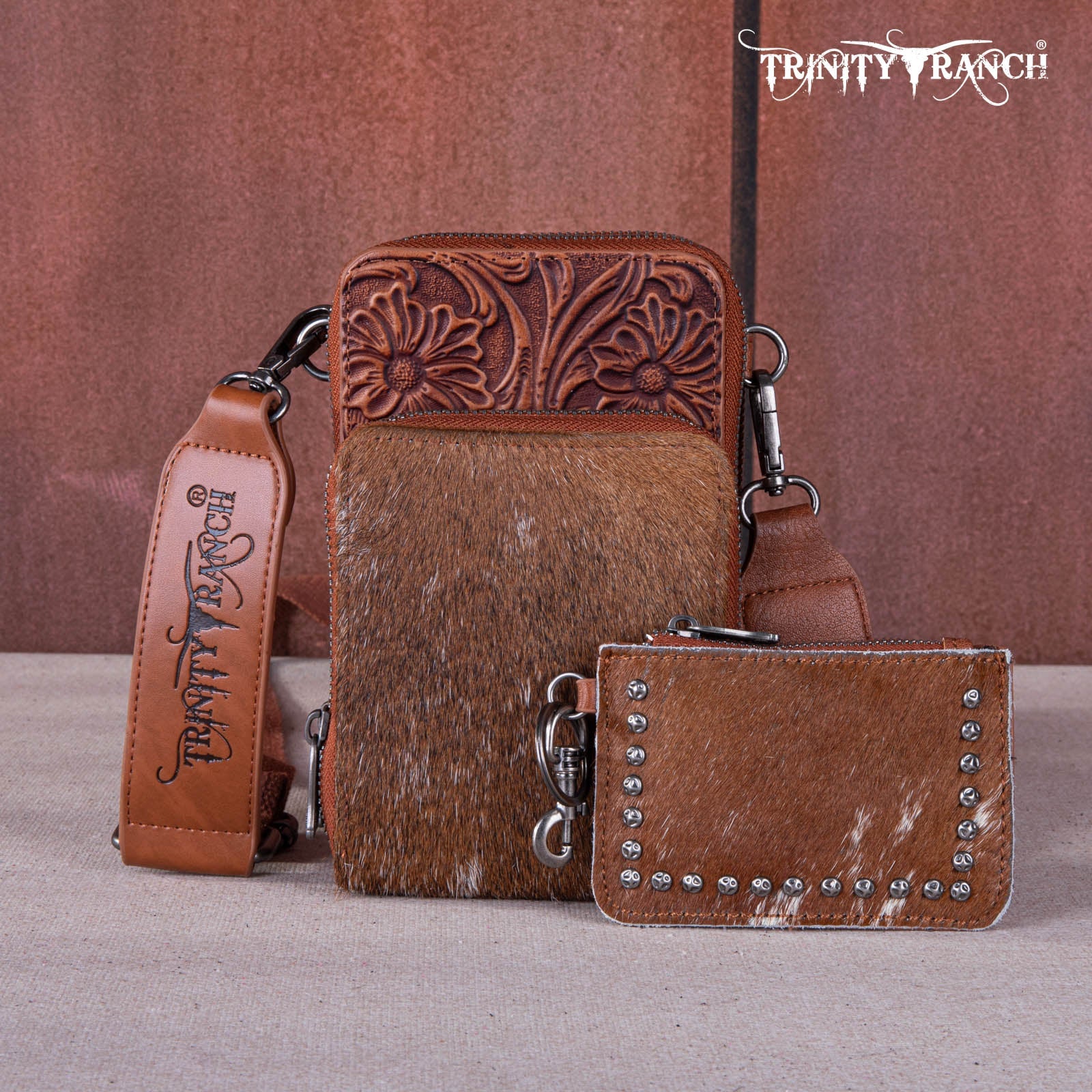 Brown leather wallet with embossed design and keychain on a textured surface, featuring 'Trinity Ranch' branding.