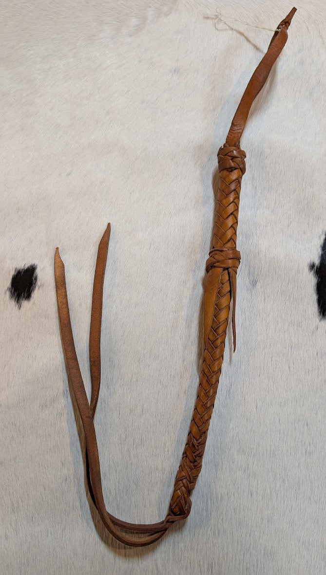 Tan leather whip on a cowhide rug with black spots