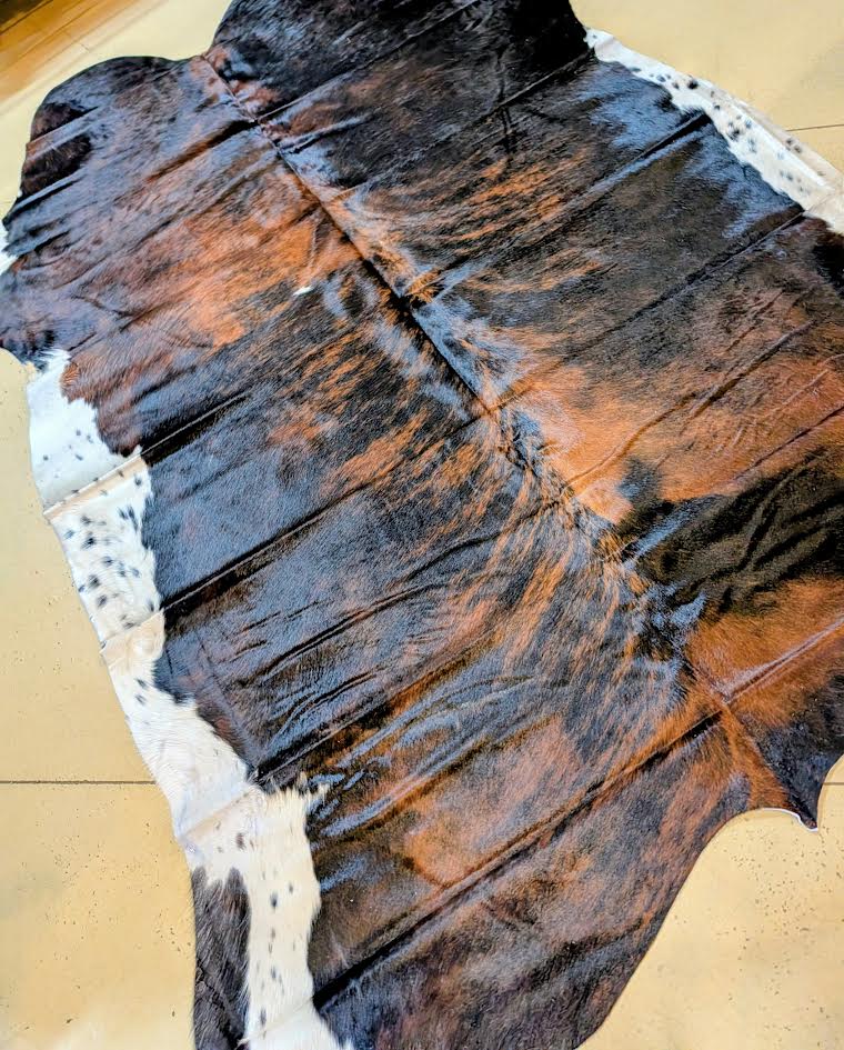 Black, brown, white cowhide rug with a beige floor.
