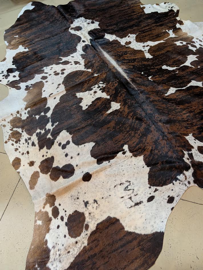 Cowhide rug with brindle and white  on a tan floor.