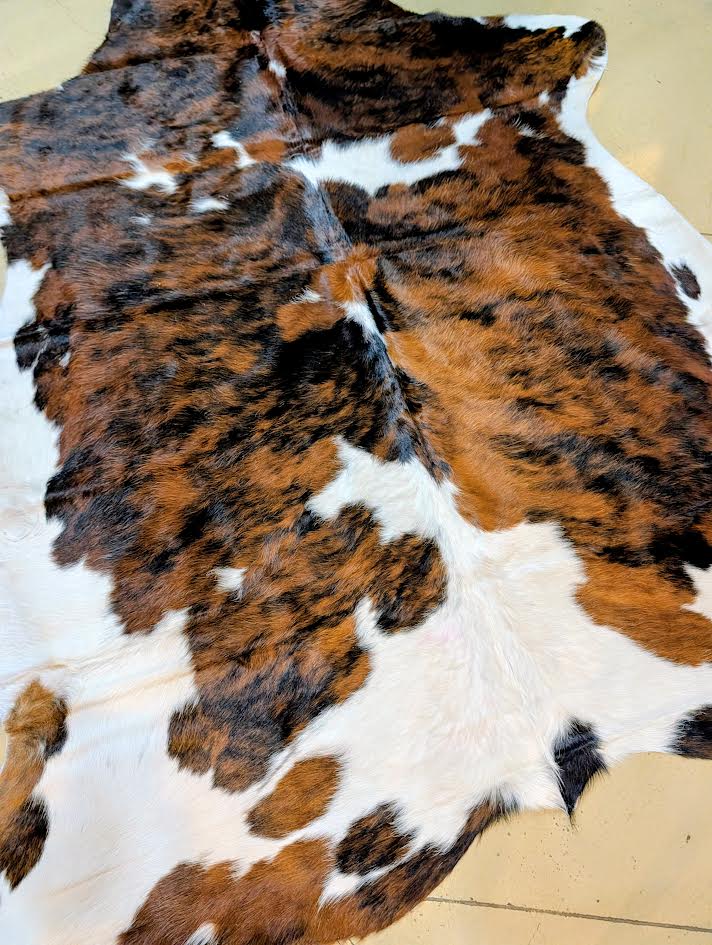 Brown, black, and white cowhide rug on a beige floor.